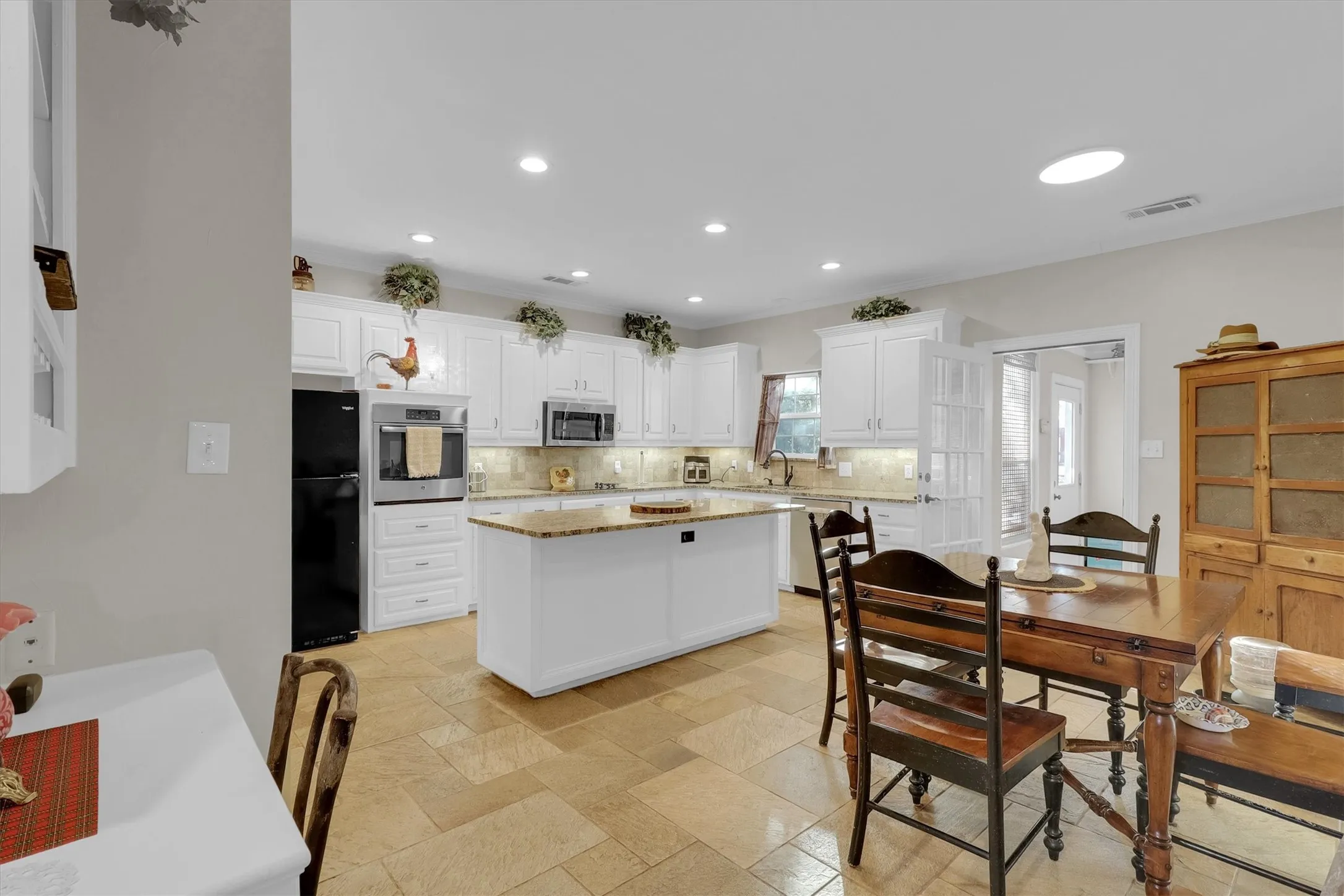 Kitchen featuring white cabinets, light stone countertops, stainless steel appliances, a kitchen island, and tasteful backsplash