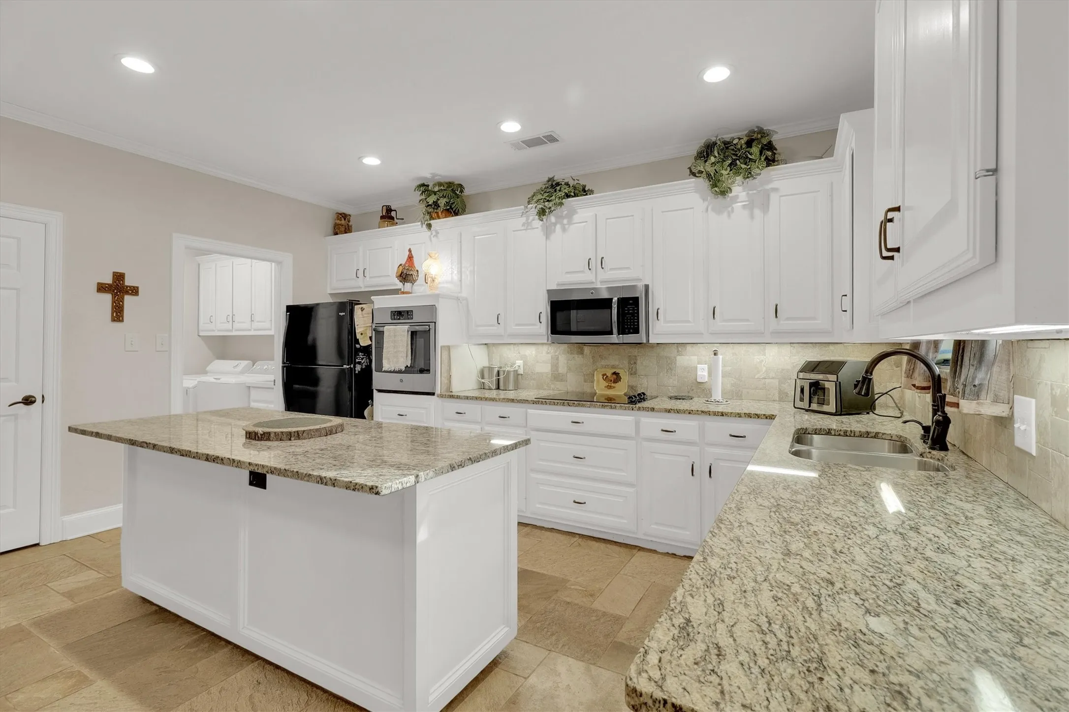 Kitchen featuring white cabinetry, black appliances, light stone counters, tasteful backsplash, and a center island