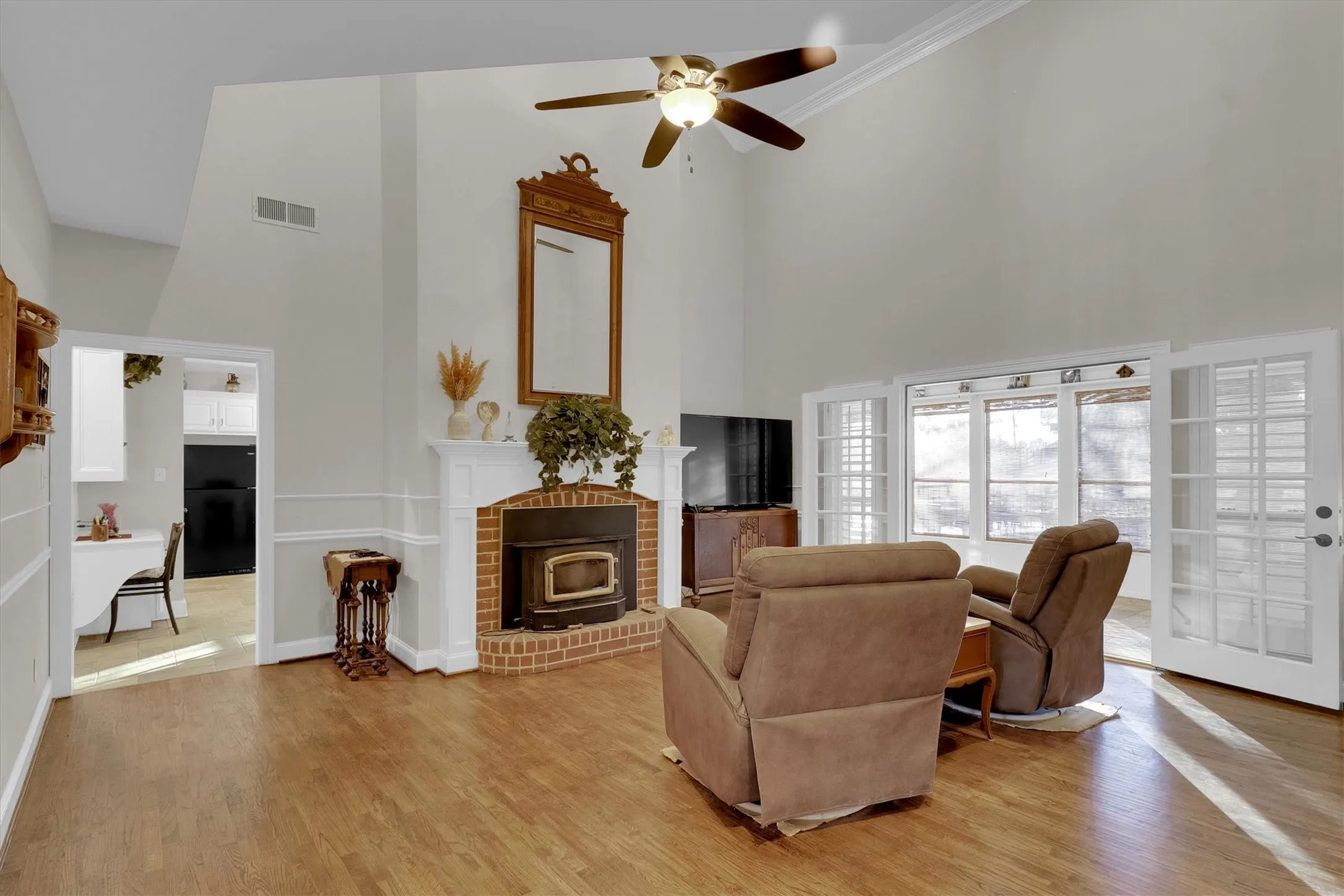 Living area with a towering ceiling, a wood stove, light wood-type flooring, and ceiling fan