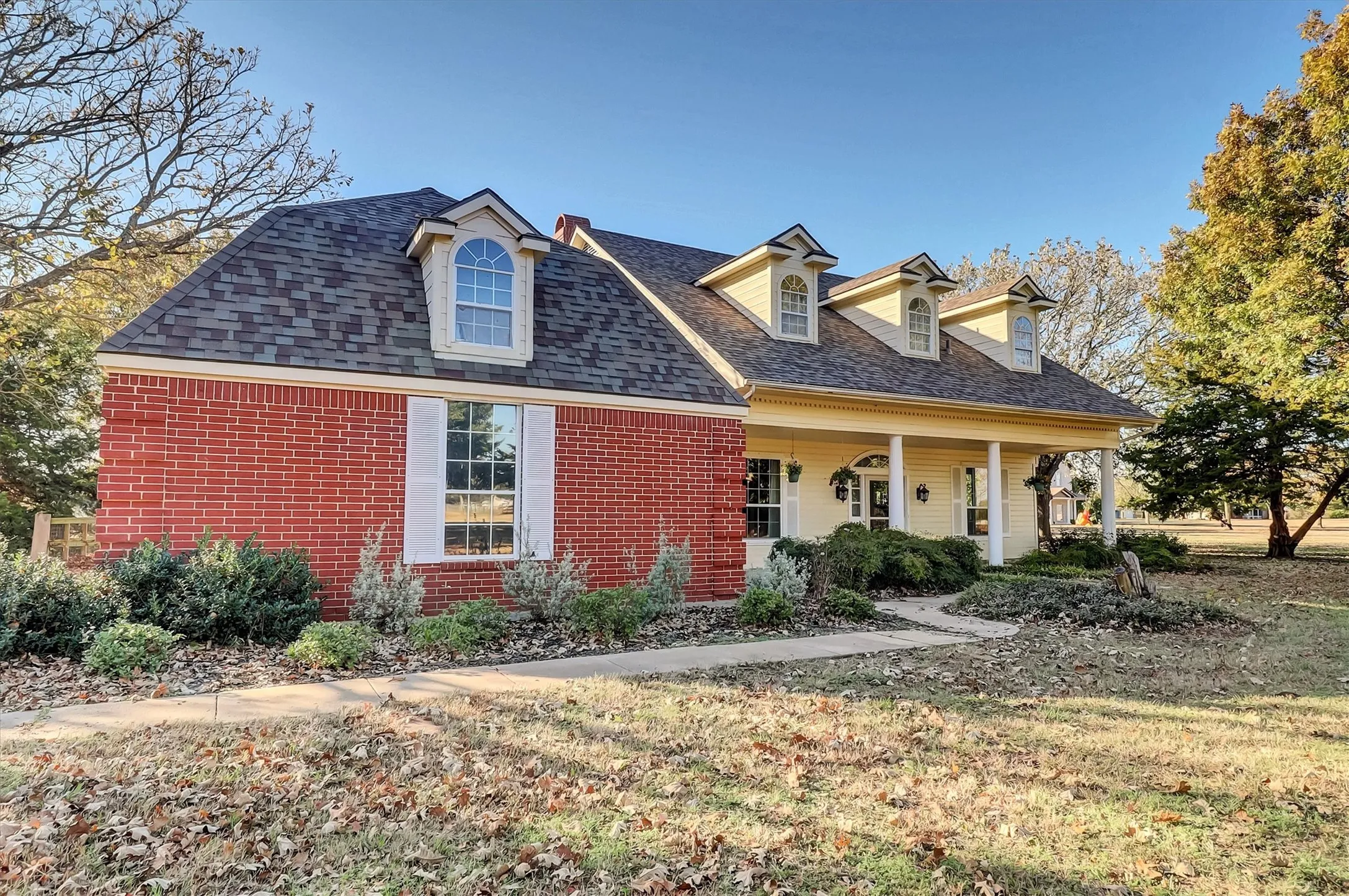 View of front facade with covered porch, brick siding, roof with shingles, and a front lawn