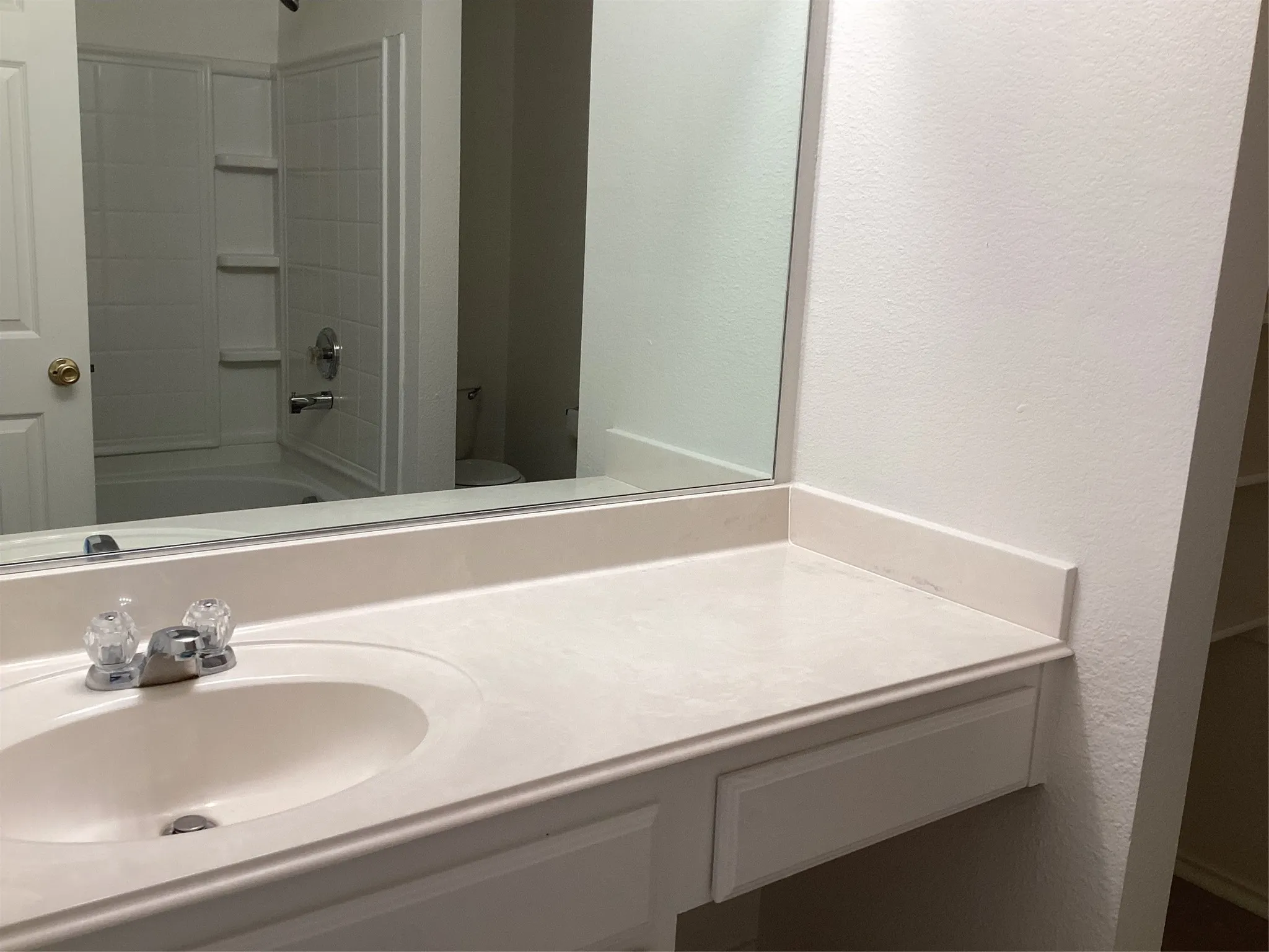 Bathroom vanity with an integrated sink, clear faucet handles, and a mirrored wall