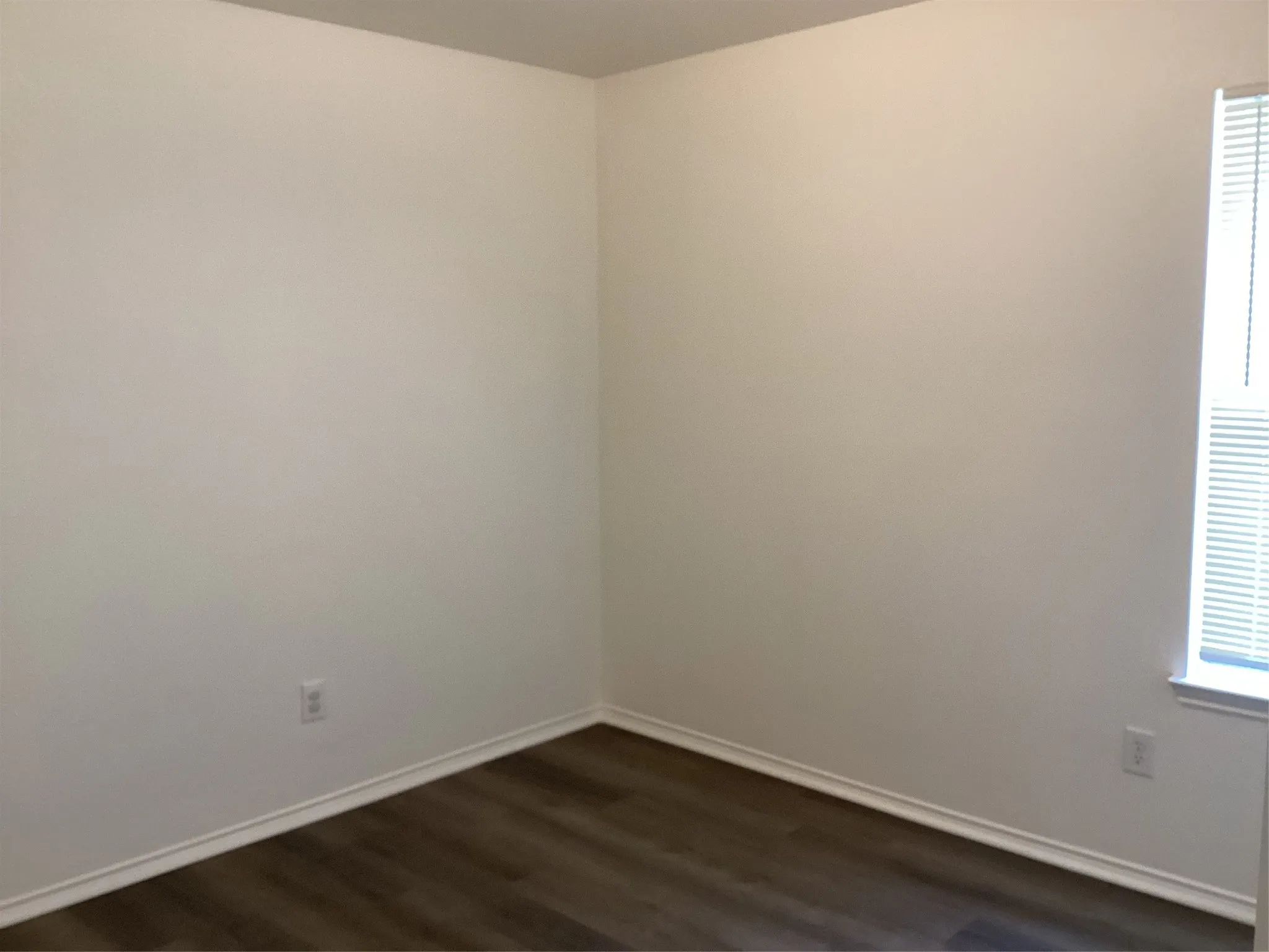 Room with wood-finish flooring, neutral wall color, white baseboards, and a window with horizontal blinds