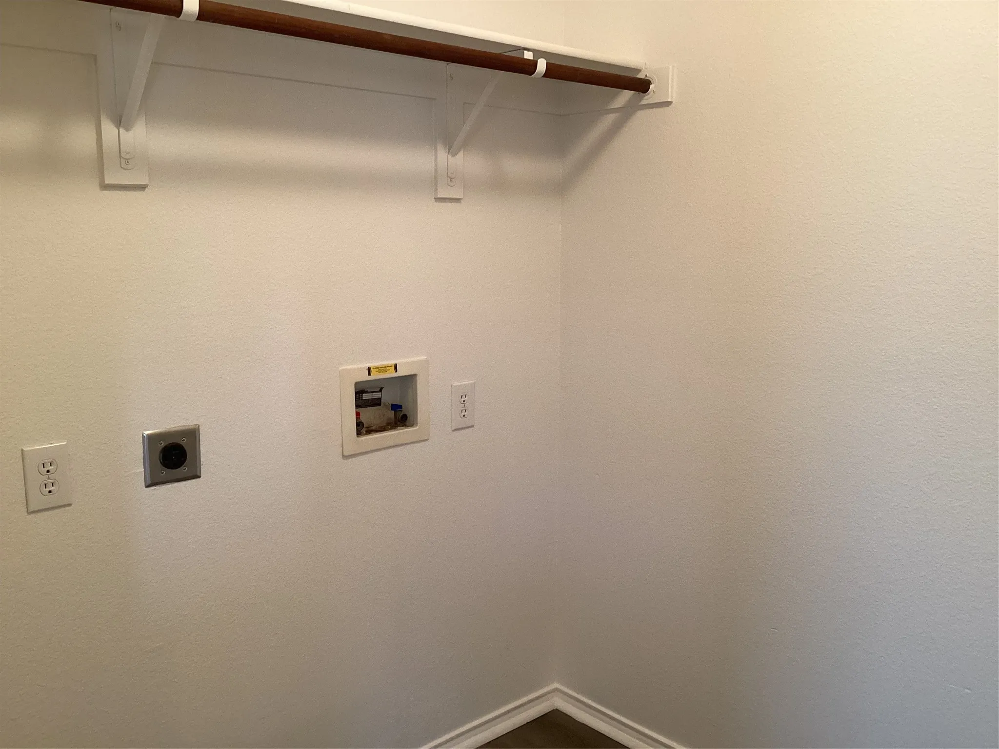 Dedicated laundry area featuring a wall-mounted shelf with a hanging rod, 240V outlet, and water hookups for appliances