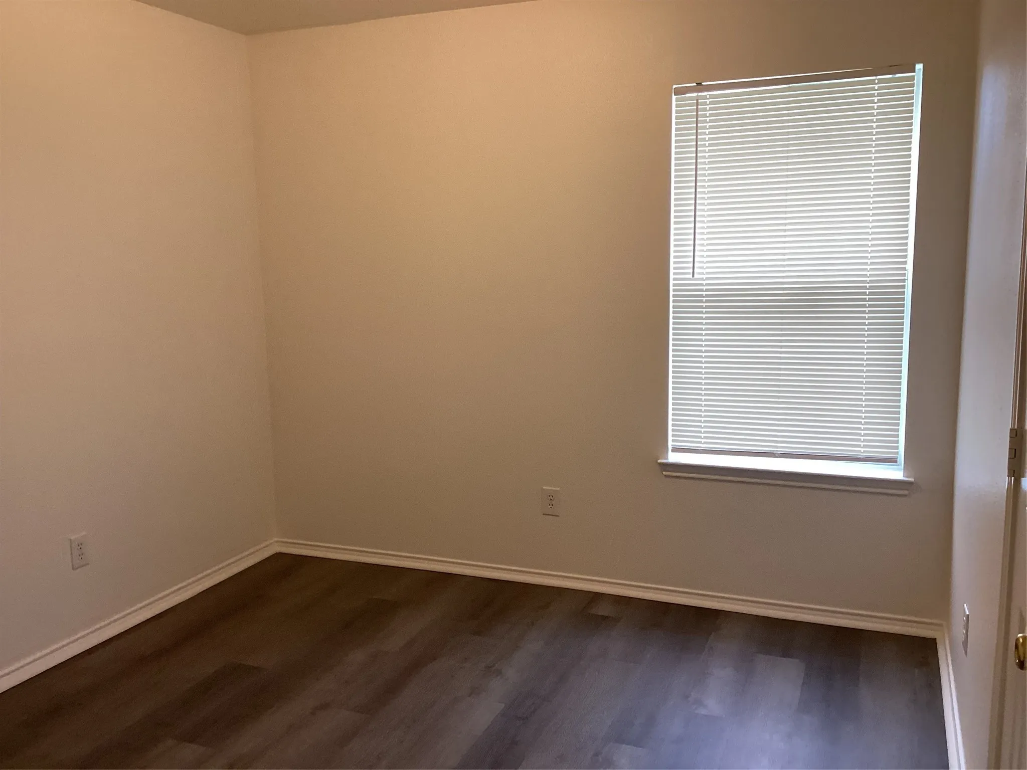 Window-equipped room featuring wood-finish flooring, light-toned walls, and white trim molding