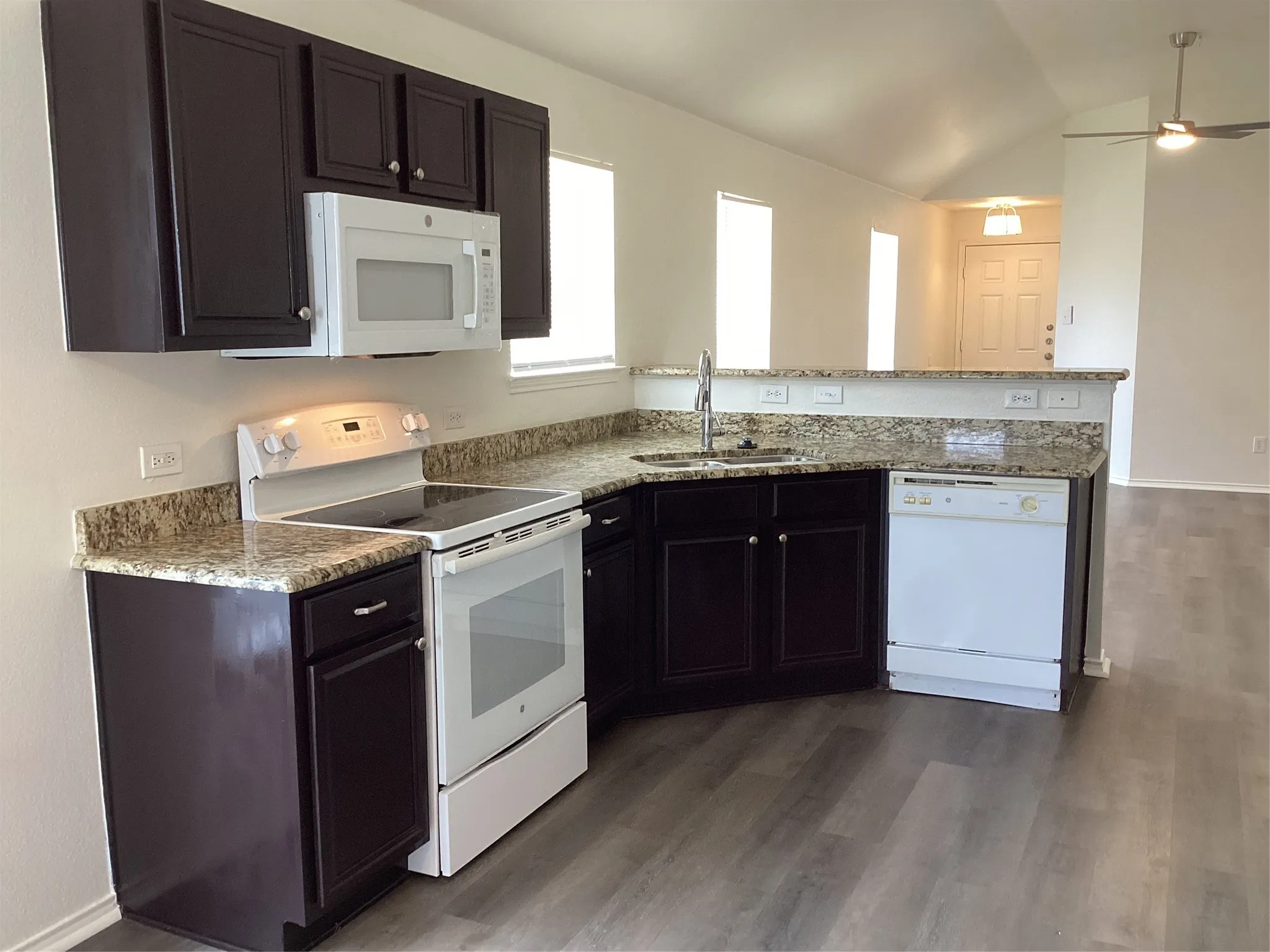 Kitchen featuring dark wood cabinetry, light-toned granite countertops, and white appliances including a built-in microwave, electric range, and dishwasher