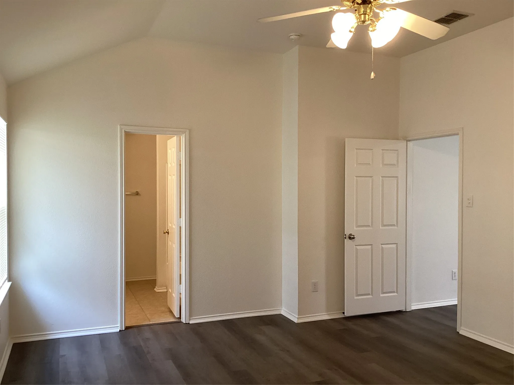 Spacious room featuring vaulted ceilings, wood-finish flooring, and a ceiling fan