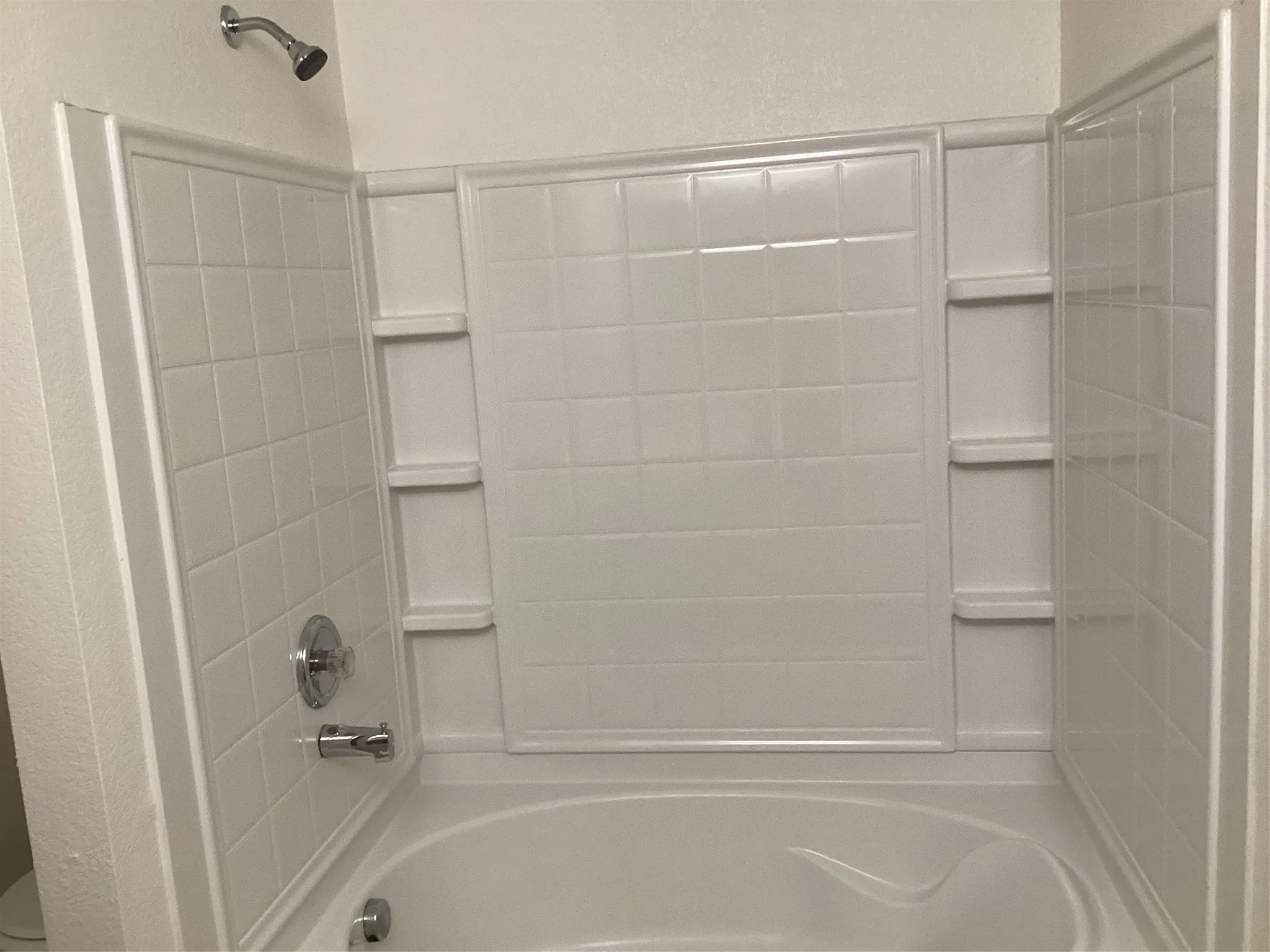 White fiberglass tub and shower combination with chrome fixtures, featuring a built-in shower caddy