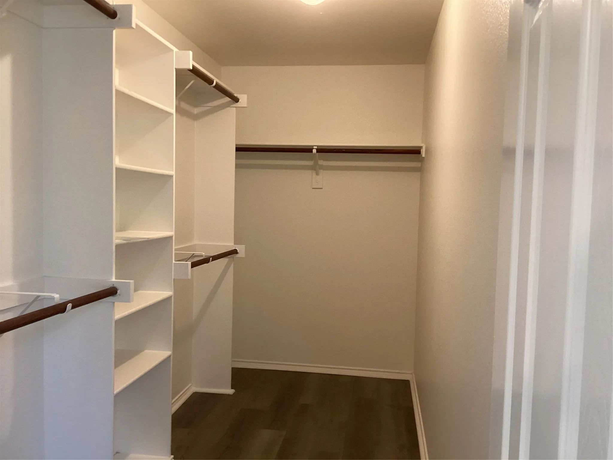 Walk-in closet featuring built-in shelving, multiple hanging rods, and wood-finish flooring