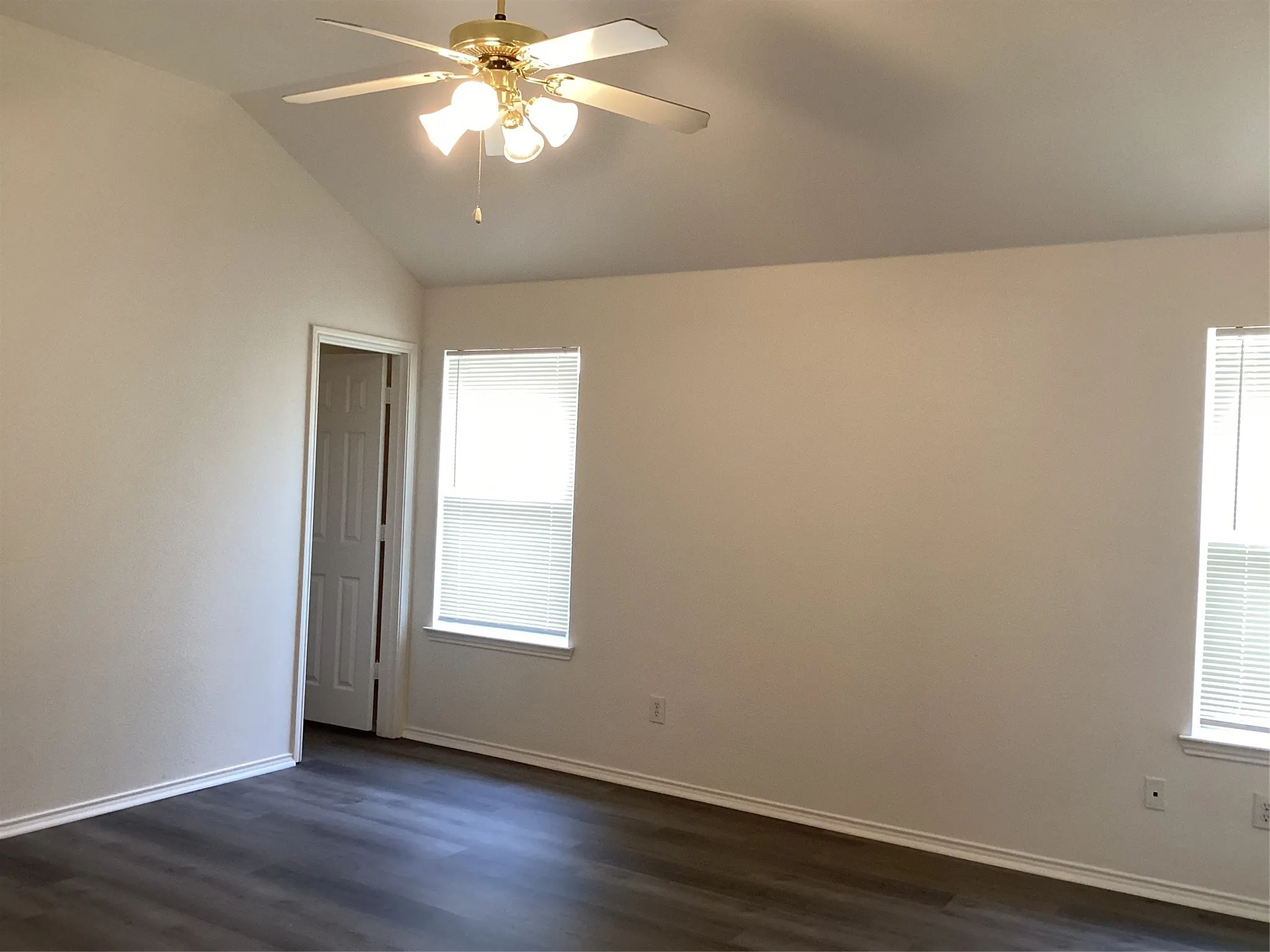 Vaulted ceiling with a ceiling fan light fixture, wood-finish flooring, and two windows featuring blinds