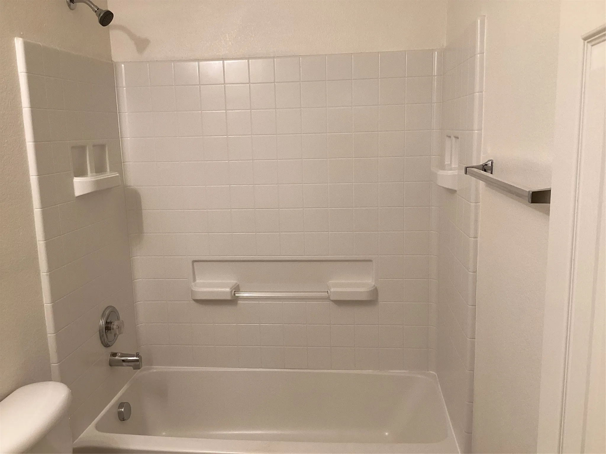 White tile shower surround with integrated shelving and a chrome shower head