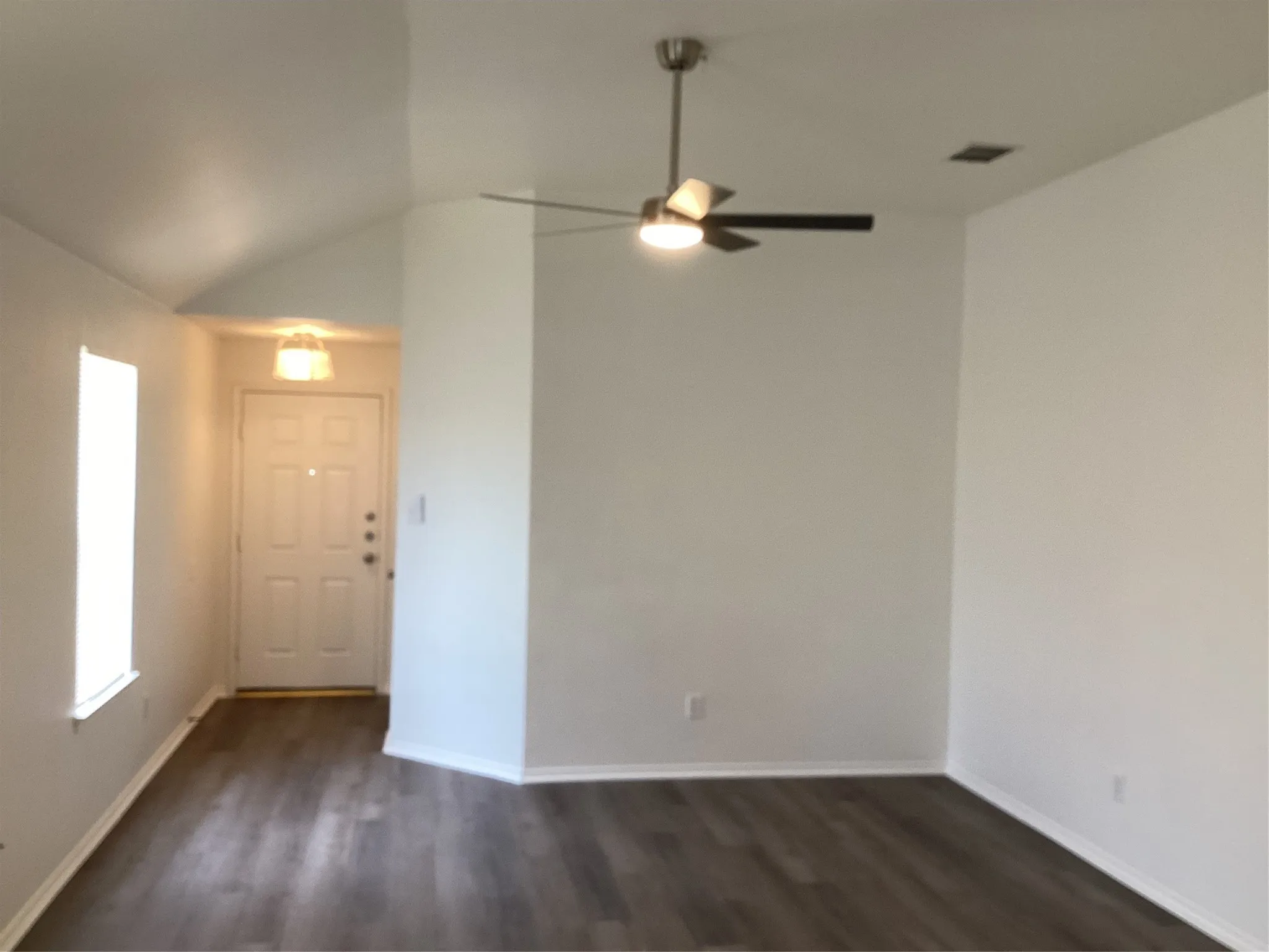 Spacious interior featuring wood-finish flooring, a contemporary ceiling fan with integrated lighting, and a vaulted ceiling