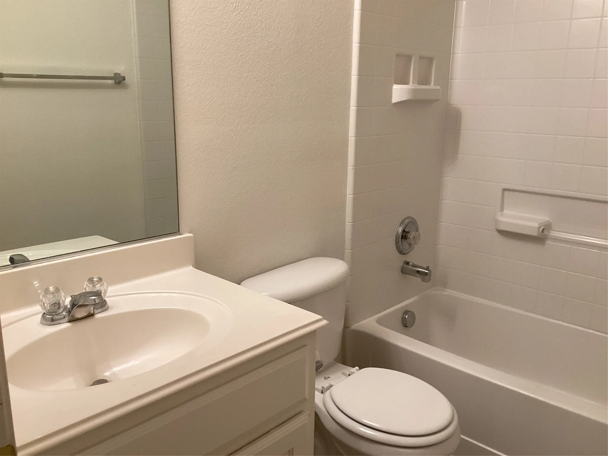 Full bathroom featuring a white vanity with integrated sink, clear knob faucets, and an expansive wall mirror