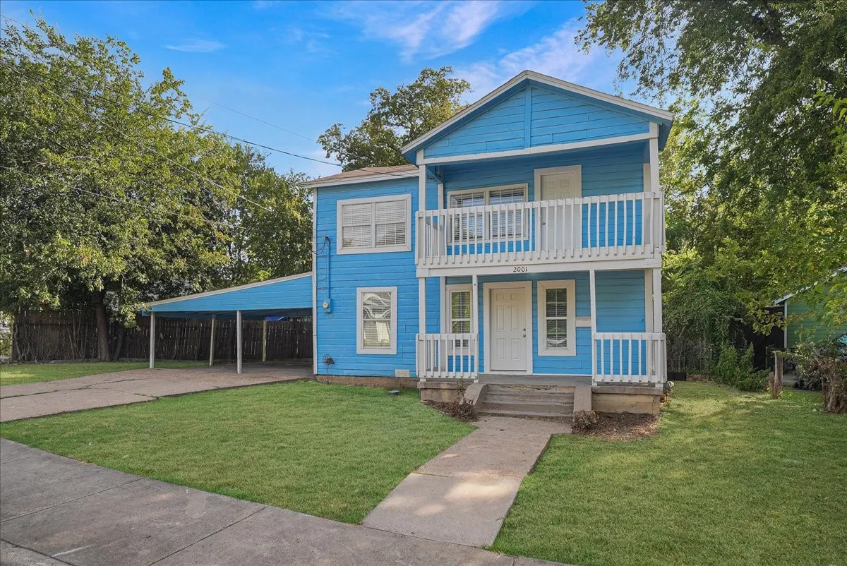 Two-story exterior with a covered upper-level balcony, ground-level porch, and a dedicated carport