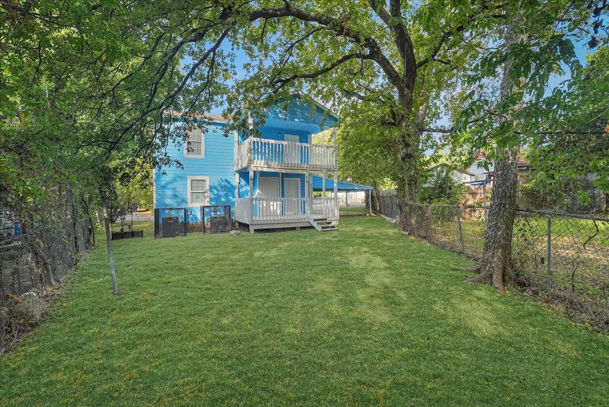 Expansive green lawn, mature trees, chain-link fencing, two-story exterior with two balconies, and a ground-level porch