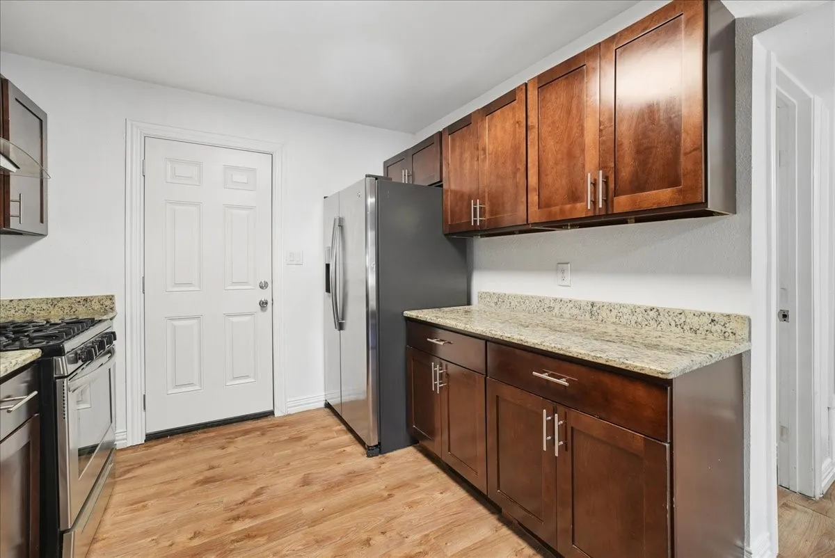 Kitchen featuring wood-finish flooring, dark wood cabinetry, granite-style countertops, stainless steel appliances, and a paneled white door