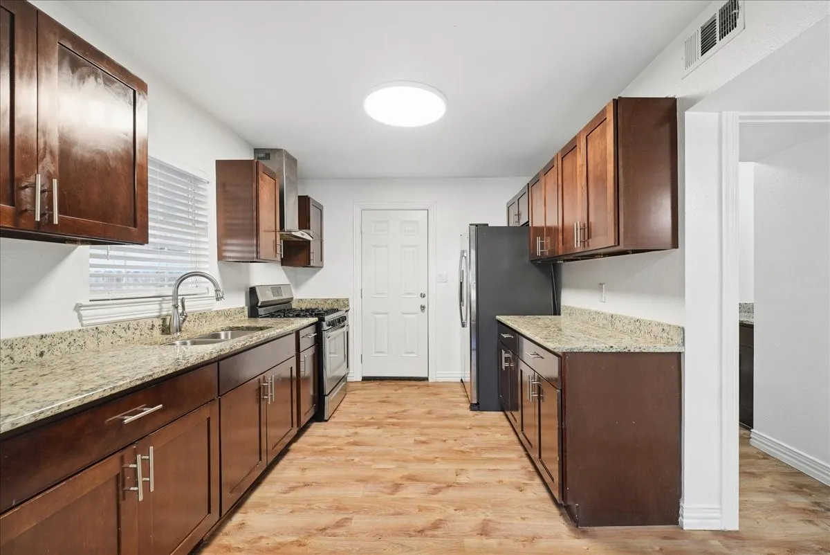 Kitchen featuring wood-finish flooring, dark wood cabinetry, light-toned countertops, and a stainless steel sink with a gooseneck faucet