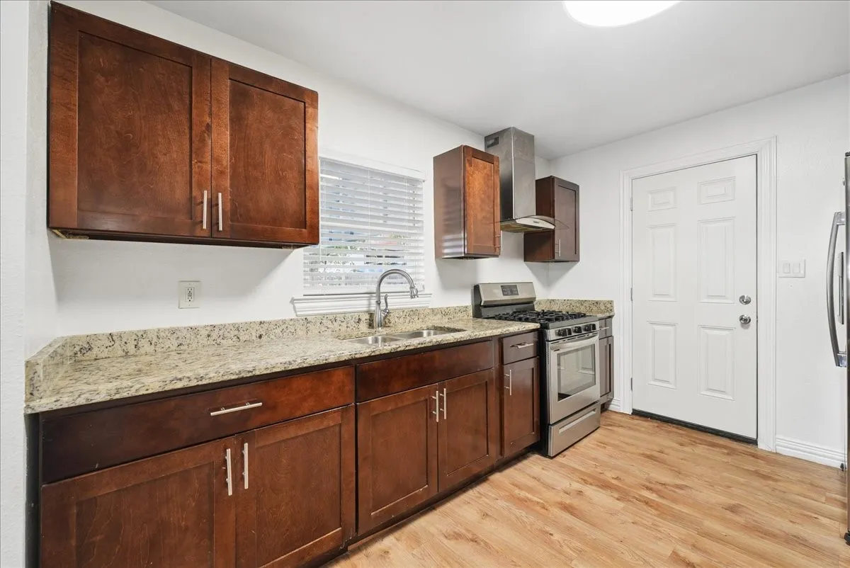 Wood-finish flooring, dark wood cabinetry, light granite countertops, stainless steel appliances, and a stainless steel range hood