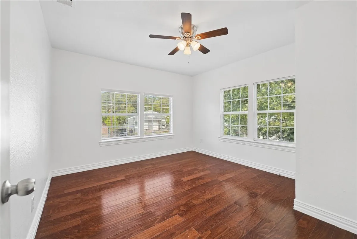 Hardwood-style flooring, white trim, multiple windows, and a ceiling fan
