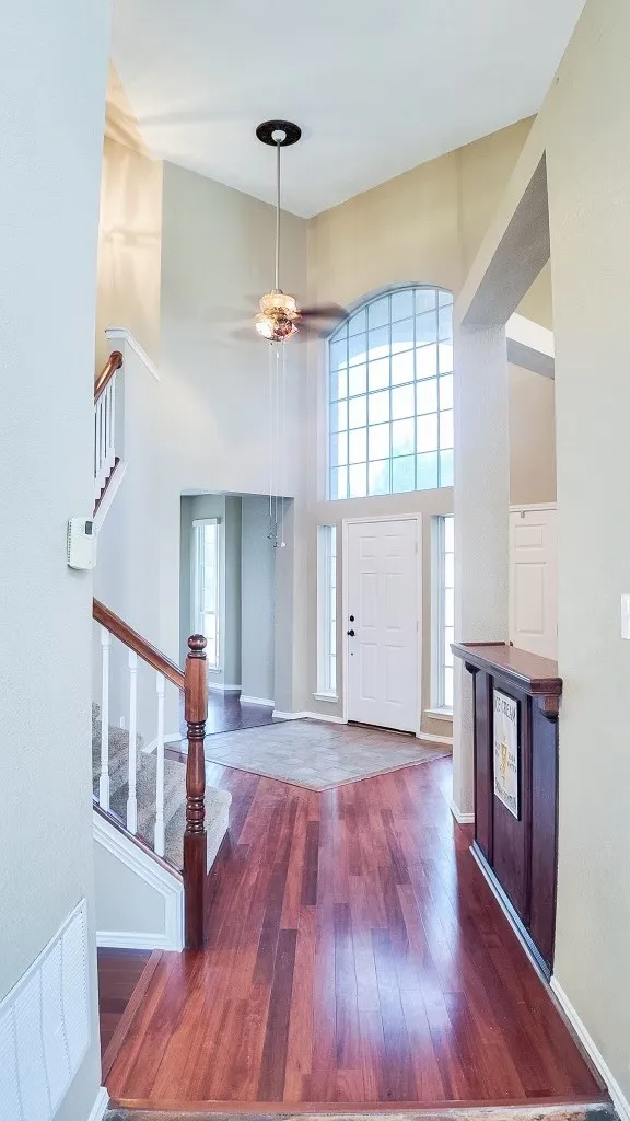 Two-story foyer featuring wood-finish flooring, a grand arched window, a ceiling fan with light fixture, an interior staircase with wood newel posts, and a built-in wood-paneled bar