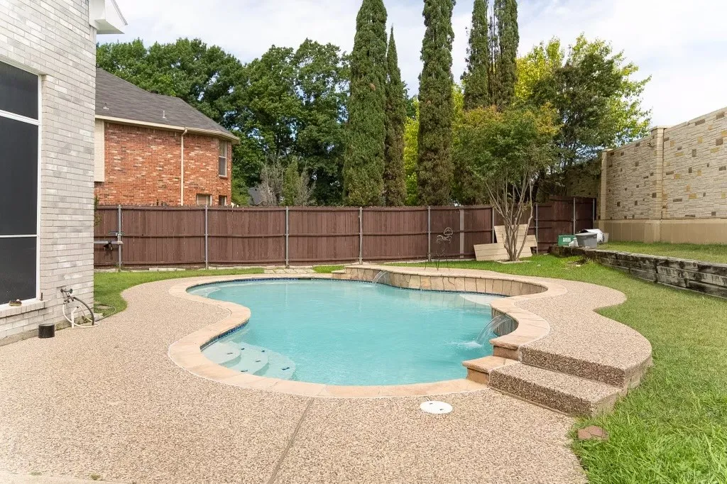 Outdoor swimming pool with integrated spa and waterfall feature, surrounded by an exposed aggregate patio