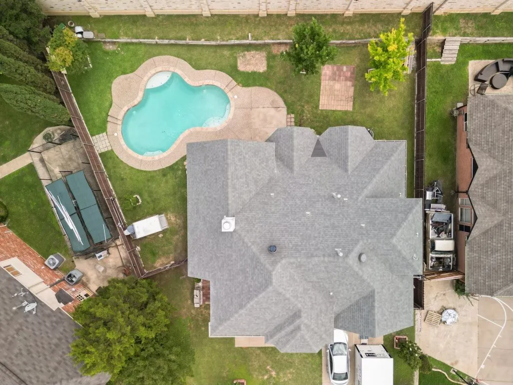 Rear yard featuring an irregular-shaped swimming pool with stone coping, concrete patio surround, and mature landscaping