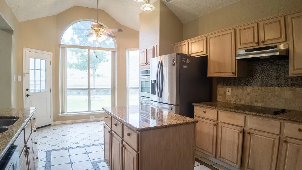 Kitchen featuring a central island with a granite countertop, light wood cabinetry, and stainless steel appliances