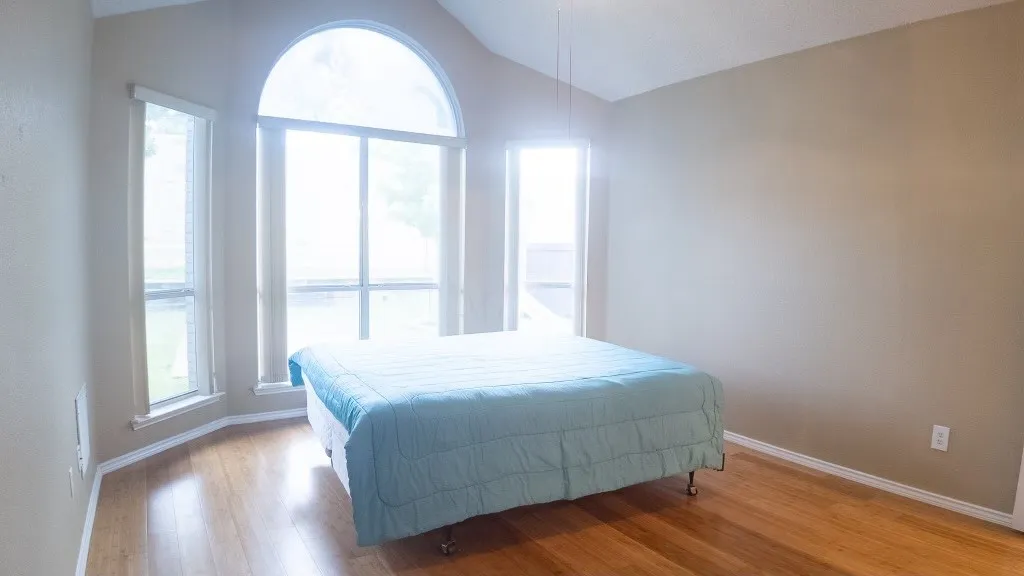 Vaulted ceiling bedroom featuring wood-finish flooring and a prominent arched window with surrounding window placements