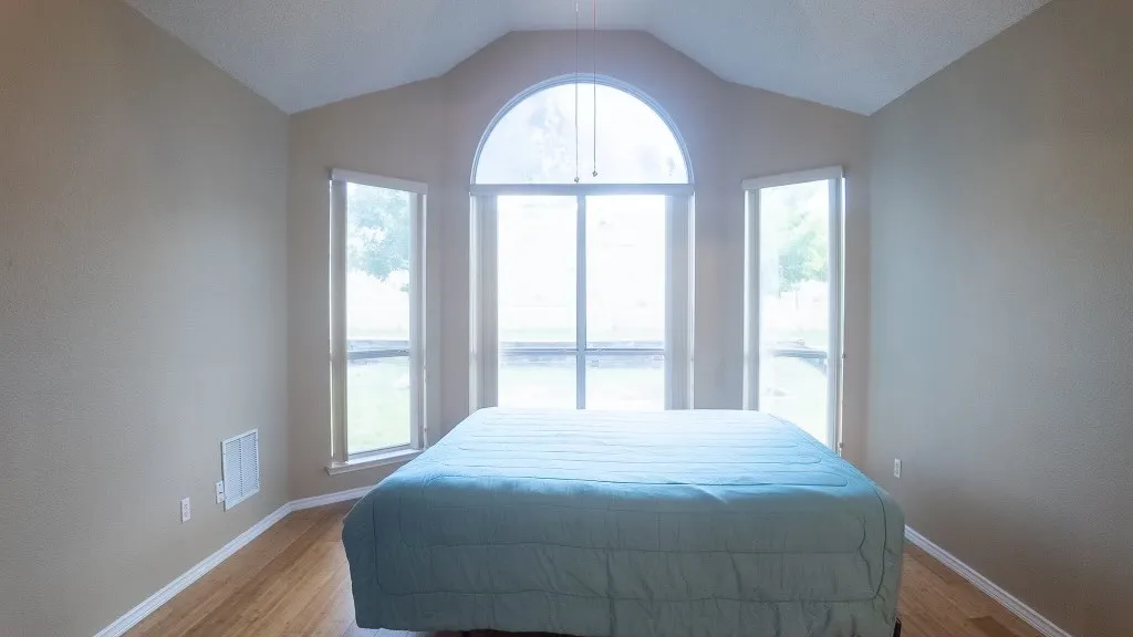 Vaulted ceiling bedroom featuring a large arched window, two vertical windows, wood-finish flooring, and neutral wall tones