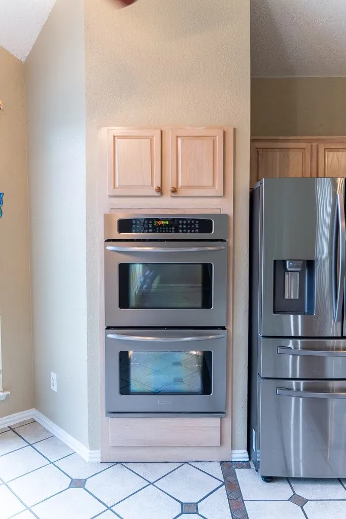 Built-in stainless steel double ovens with digital controls, flanked by light wood-finish cabinetry