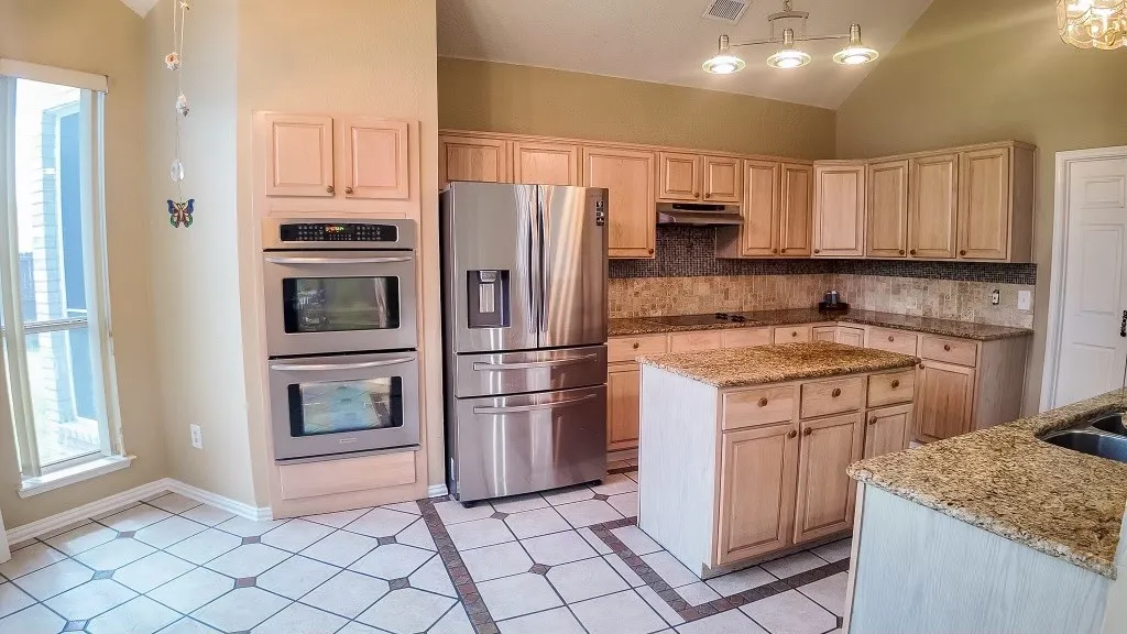 Kitchen featuring abundant wood cabinetry, stainless steel double wall ovens, a center island with countertop, and tile flooring with decorative inlay