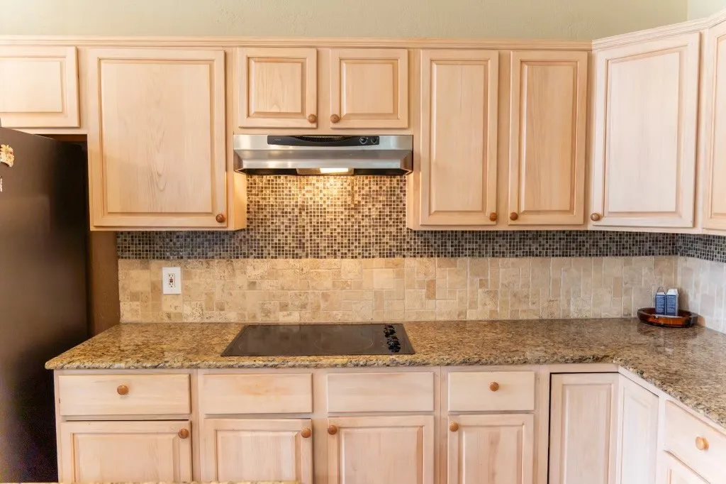 Kitchen featuring light wood cabinetry, stone countertops, a mosaic tile backsplash, and a built-in cooktop