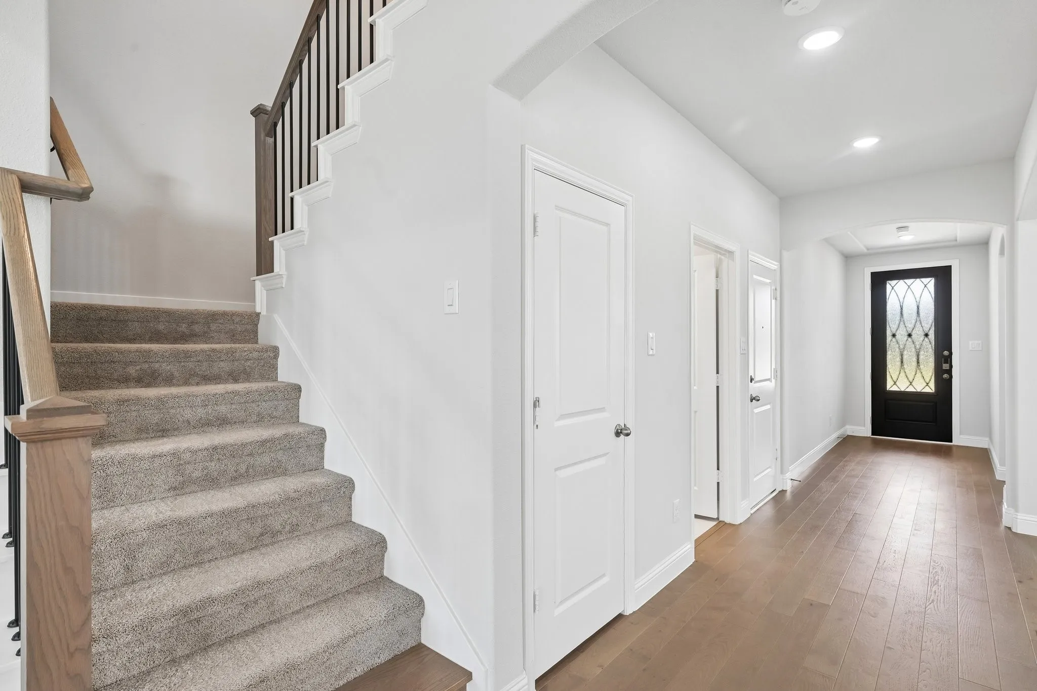 Entryway featuring wood-finish flooring, a carpeted staircase with wood handrails, a decorative front door with leaded glass, recessed lighting, and white paneled doors