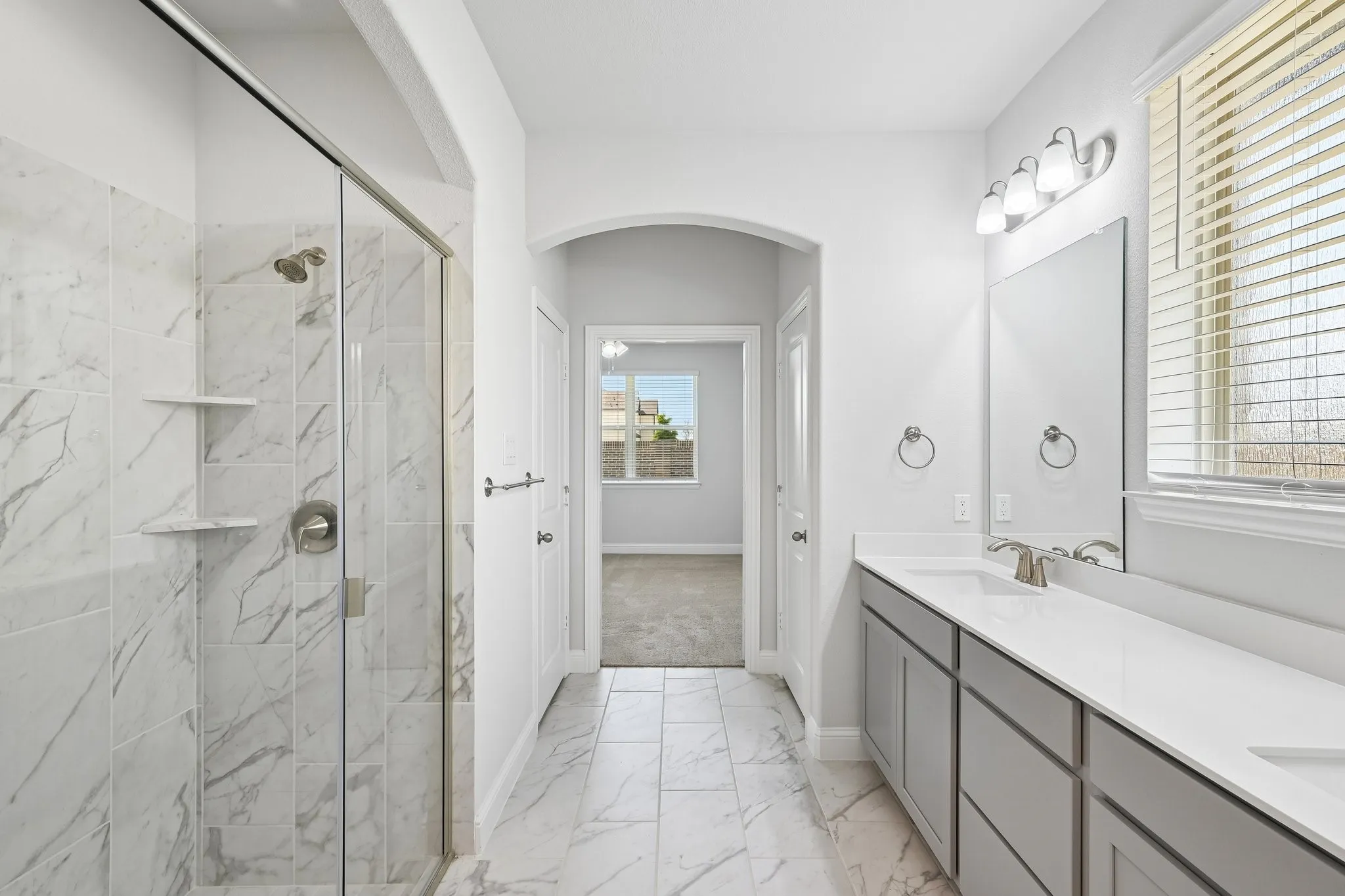 Contemporary bathroom featuring a spacious walk-in shower with glass enclosure and integrated shelving, dual vanity with undermount sinks and light-toned countertops, and marble-look tile flooring