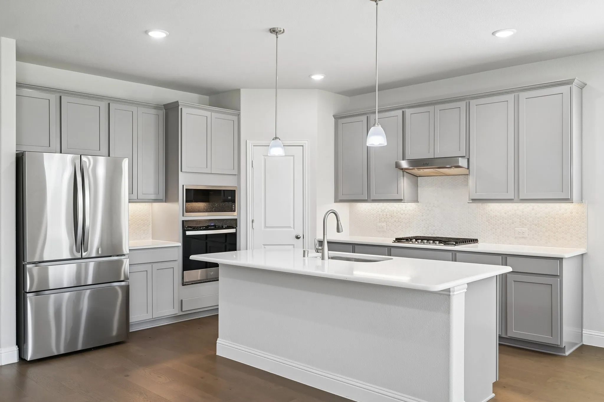 Kitchen featuring a central island with a sink, grey shaker-style cabinetry, stainless steel appliances, white countertops, and wood-finish flooring