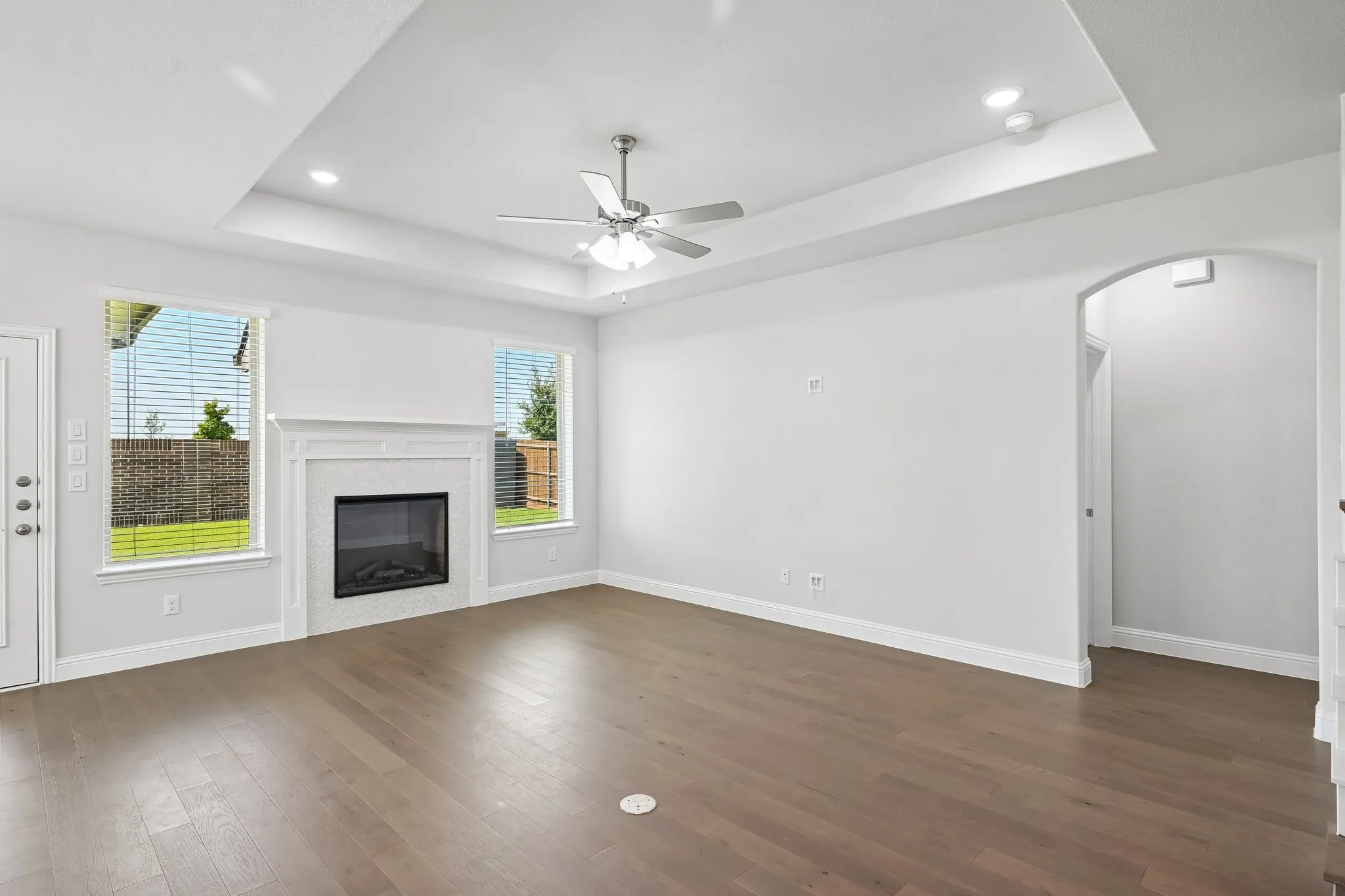 Living area featuring a tray ceiling with recessed lighting, a ceiling fan, and wood-finish flooring