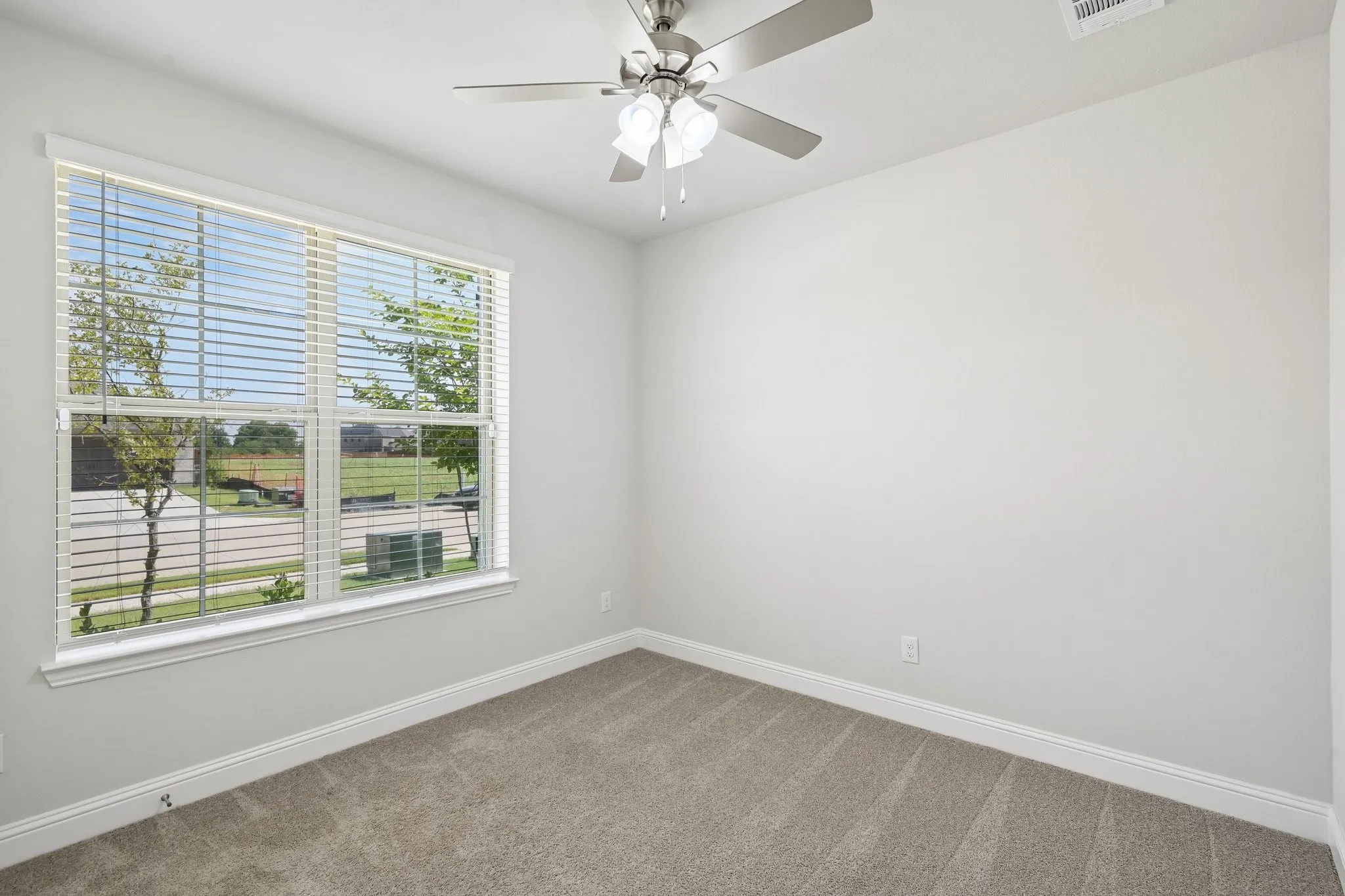 First floor secondary bedroom featuring a large window with horizontal blinds, a ceiling fan with light fixture, and white baseboards.   Can also be used as an office