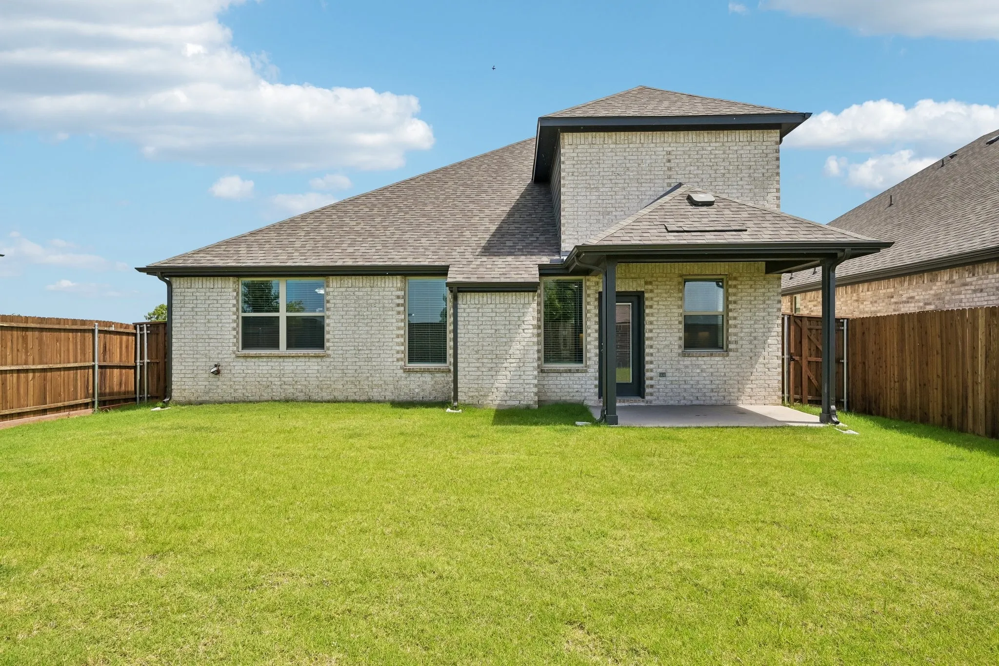 Expansive backyard featuring a manicured lawn, brick exterior, covered patio, and a privacy fence