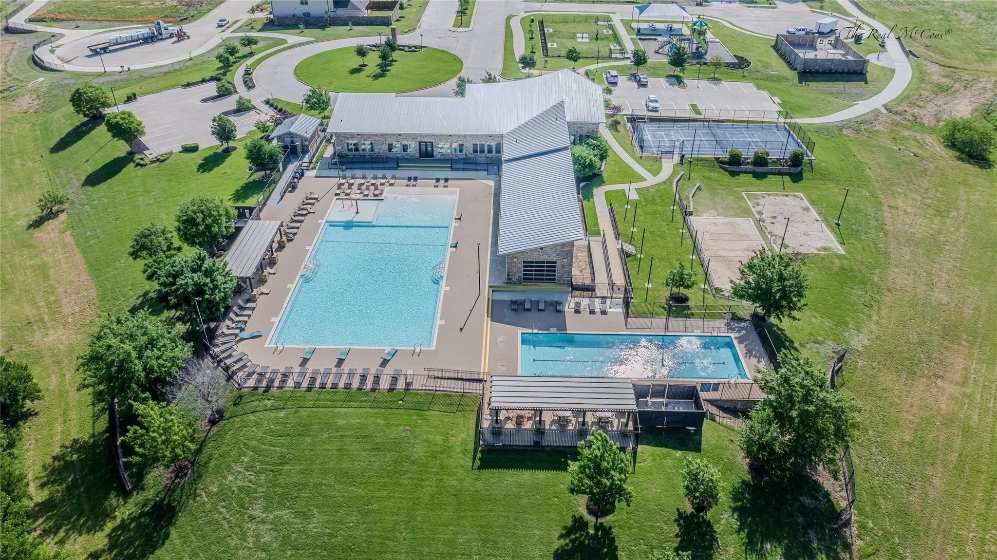 Expansive community amenity center featuring a large swimming pool, a separate lap pool, covered outdoor seating, tennis courts, and a sand volleyball court