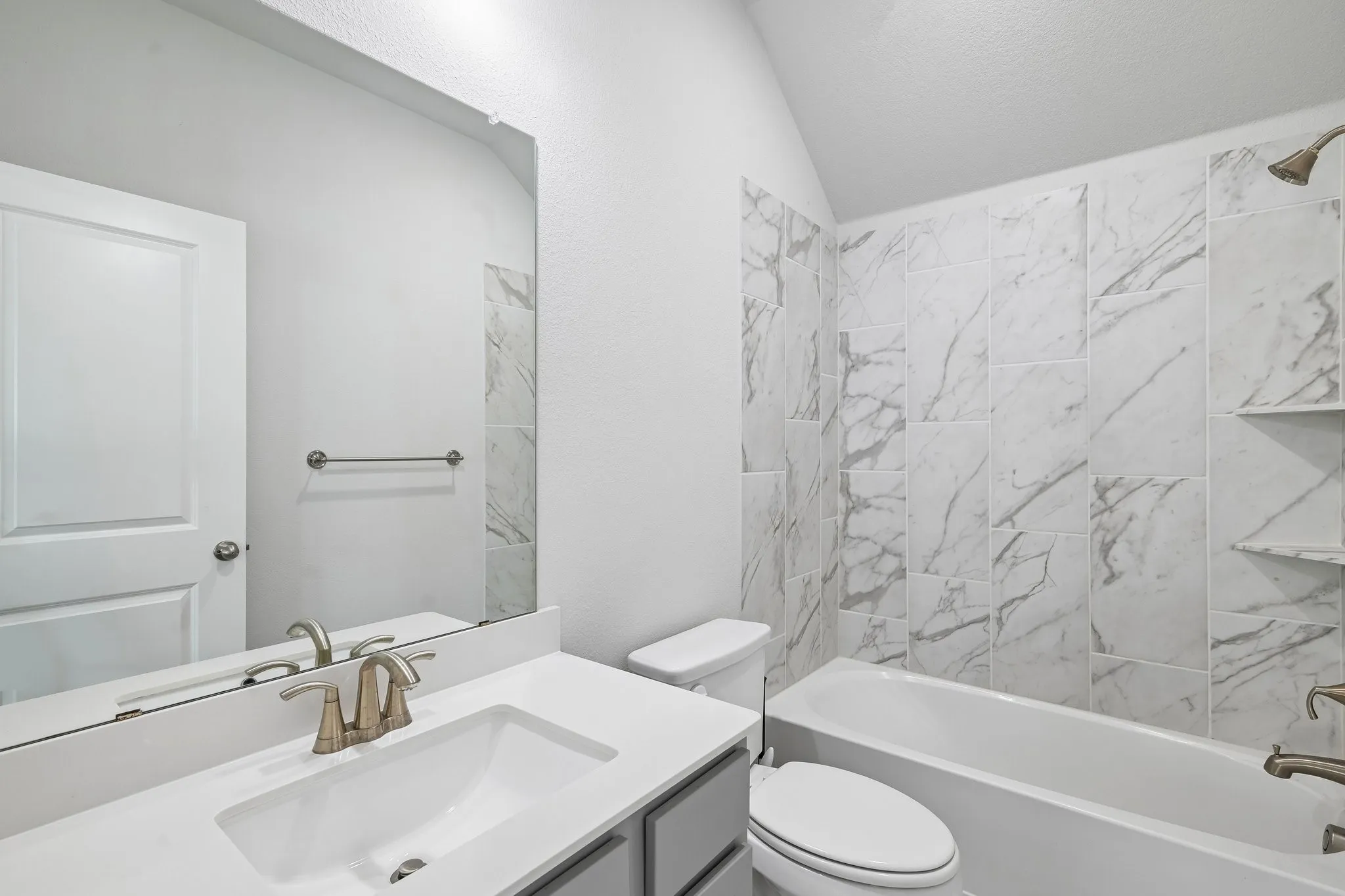 Bathroom featuring a built-in tub with a shower, patterned tile surround, and integrated shelving