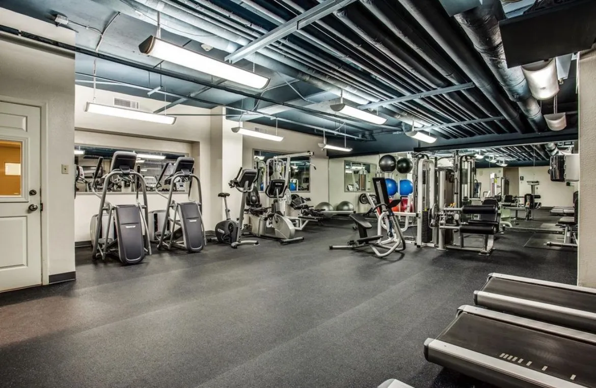 Fitness center featuring extensive cardio equipment, strength training machines, mirrored walls, rubber flooring, and exposed ceiling ductwork