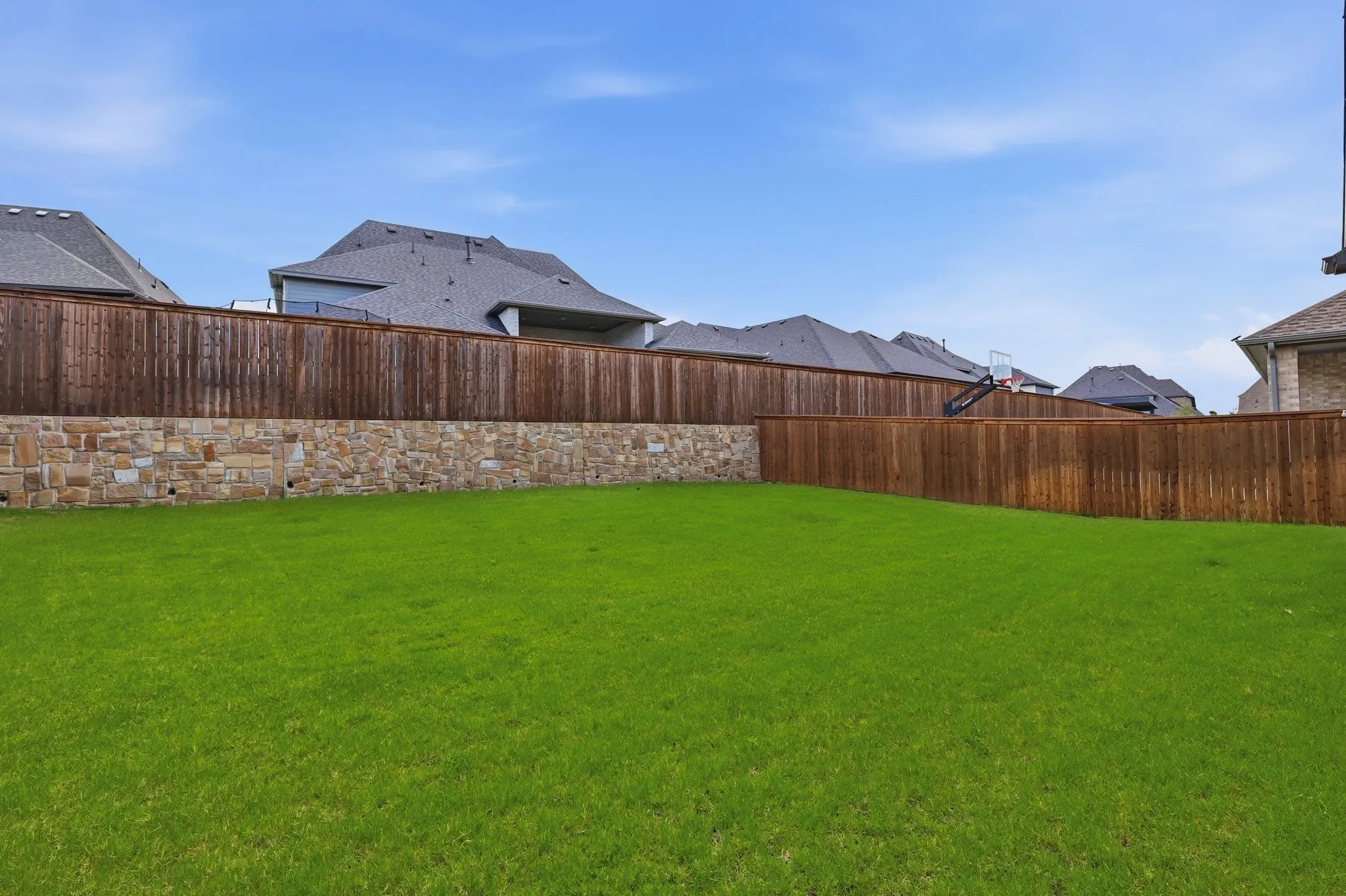 Expansive green lawn framed by a substantial wood privacy fence and a stone retaining wall