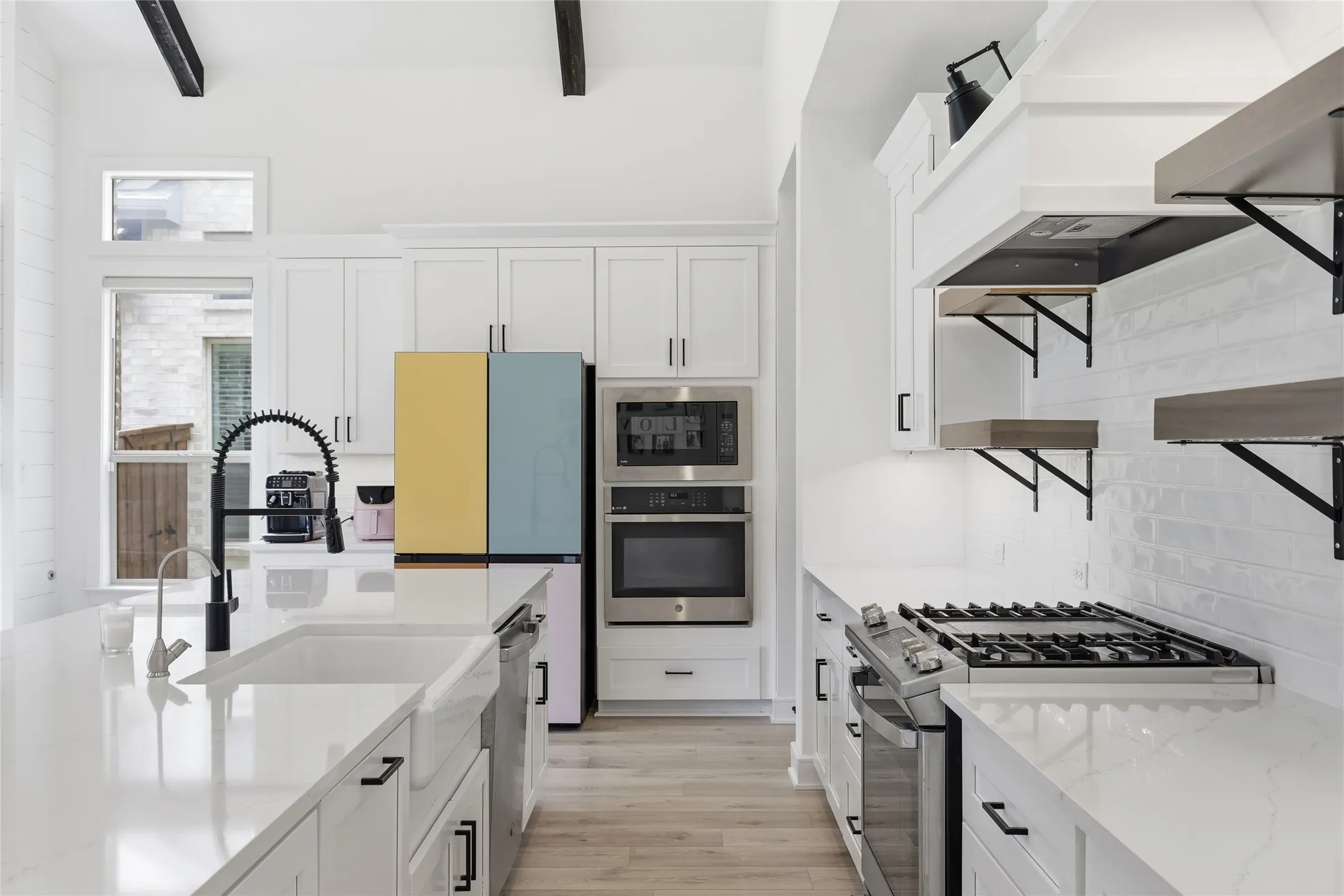 Modern kitchen featuring a large center island with an undermount sink, white cabinetry, integrated stainless steel appliances, and wood-finish flooring