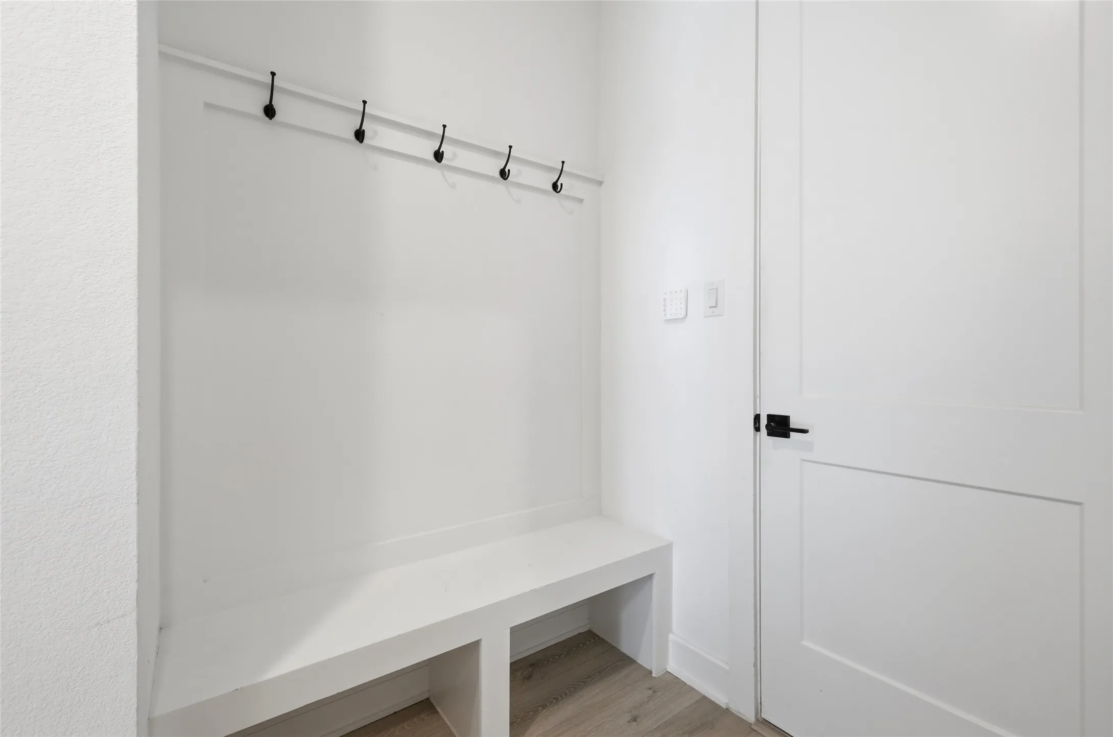 Built-in entryway bench featuring integrated storage cubbies, a coat rack with black hooks, and a paneled interior door with matte black hardware