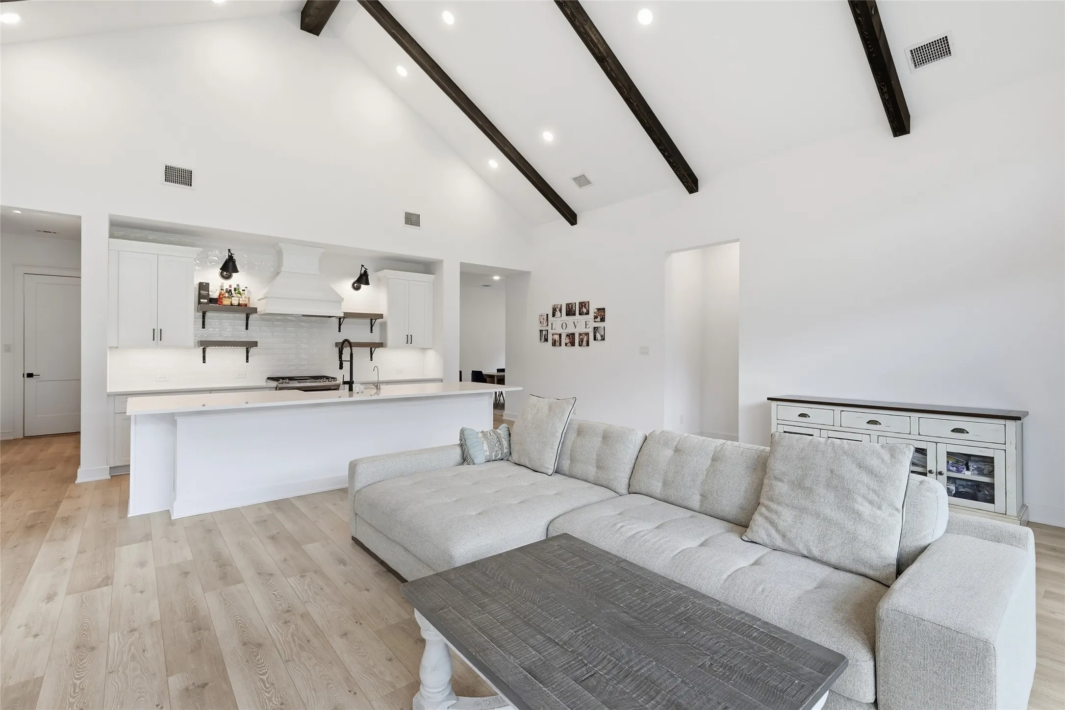 Open-concept living space featuring vaulted ceilings with exposed beams, recessed lighting, and light wood-finish flooring