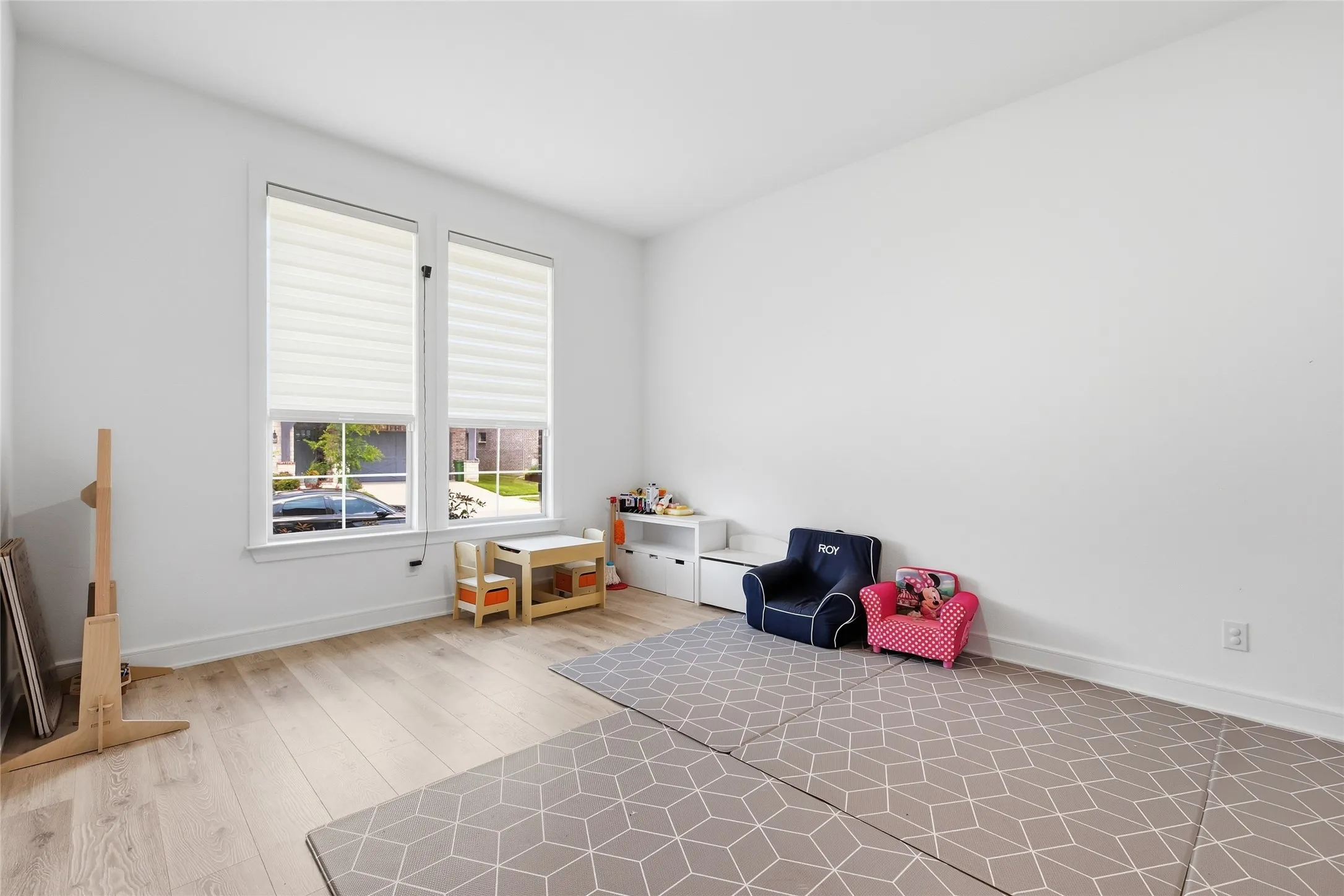 Bright room featuring two large windows with horizontal blinds, light wood-finish flooring, and white walls
