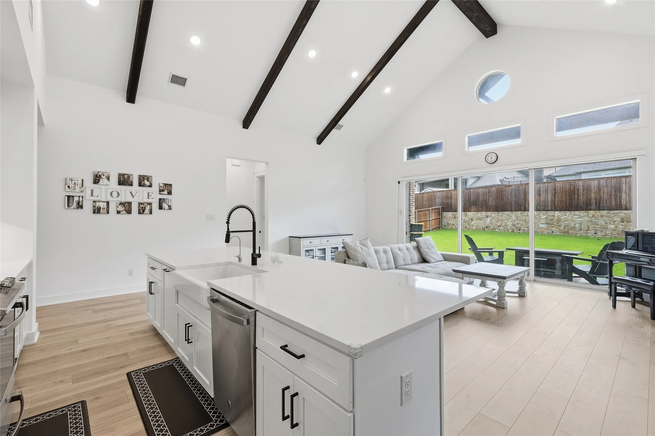 Open-concept living space featuring a vaulted ceiling with exposed beams, light wood-finish flooring, and white walls