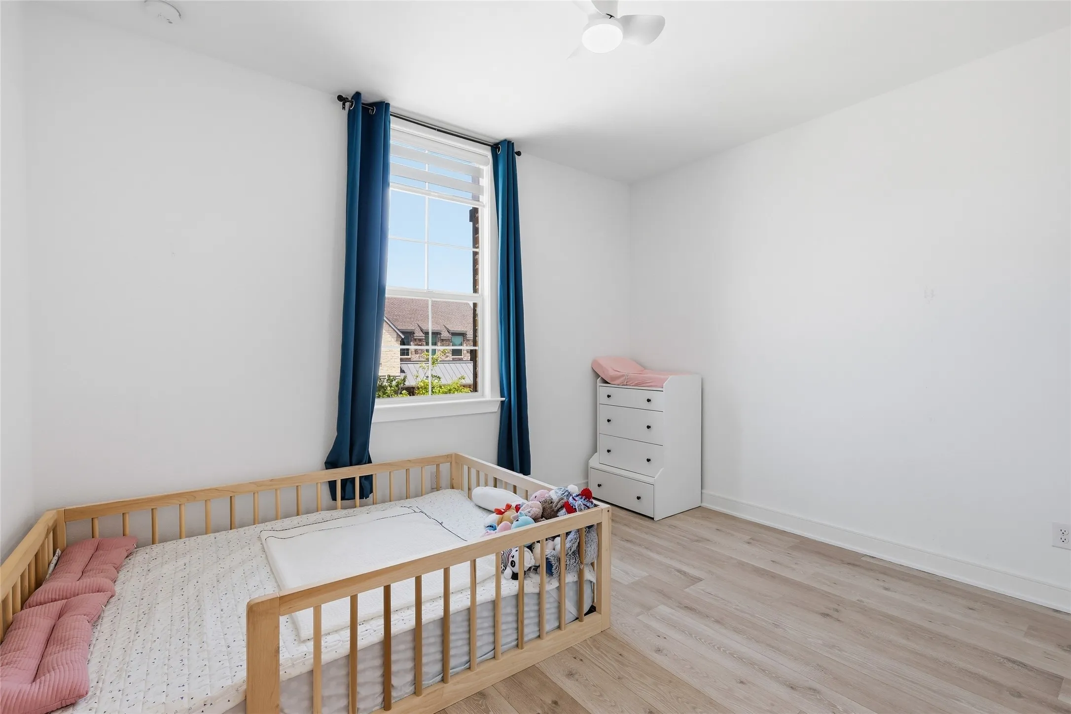 Bright room featuring light wood-finish flooring, a white ceiling fan, and a large window with white blinds