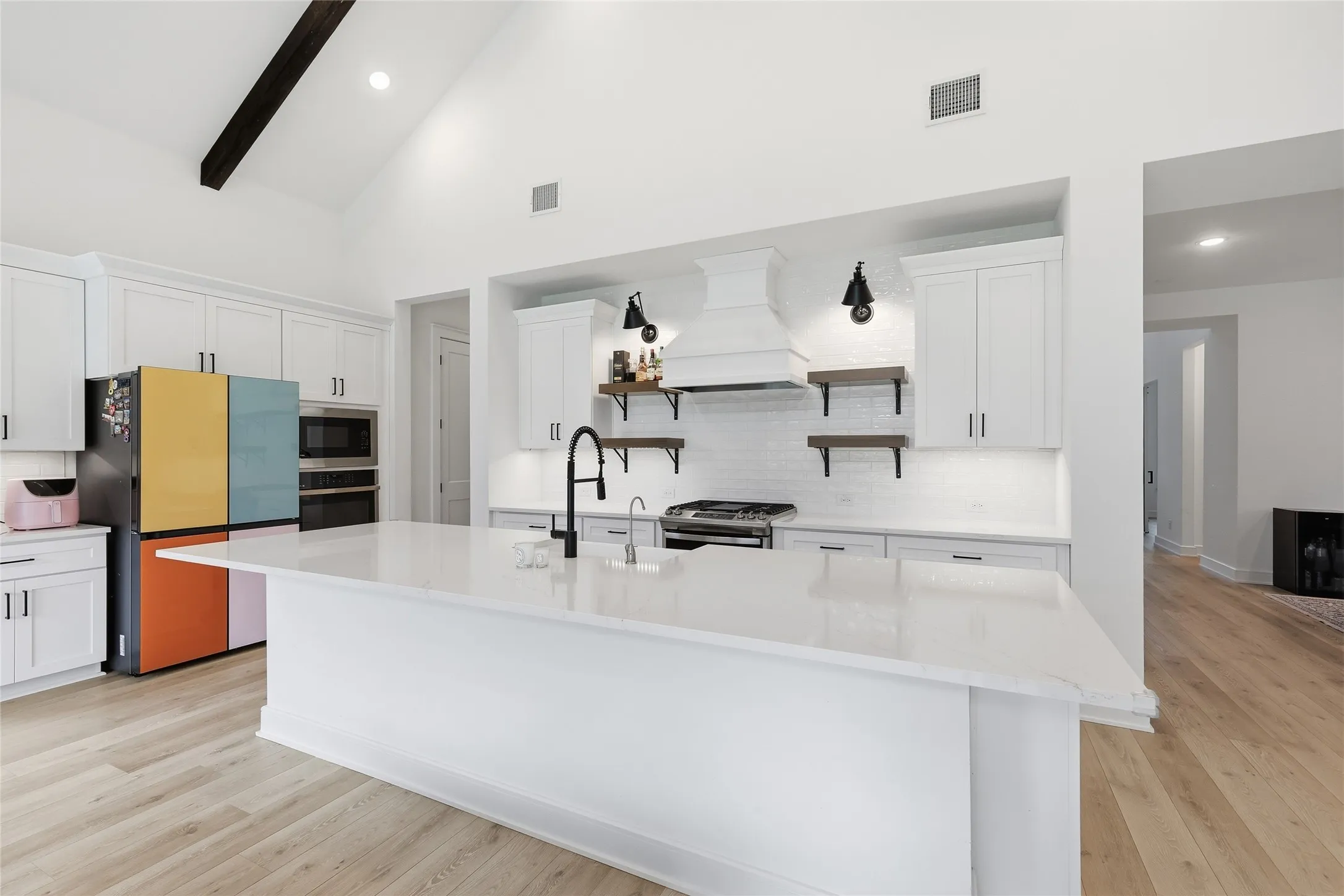 Gourmet kitchen featuring a large central island, light wood-finish flooring, white cabinetry, and vaulted ceilings with exposed wood beams