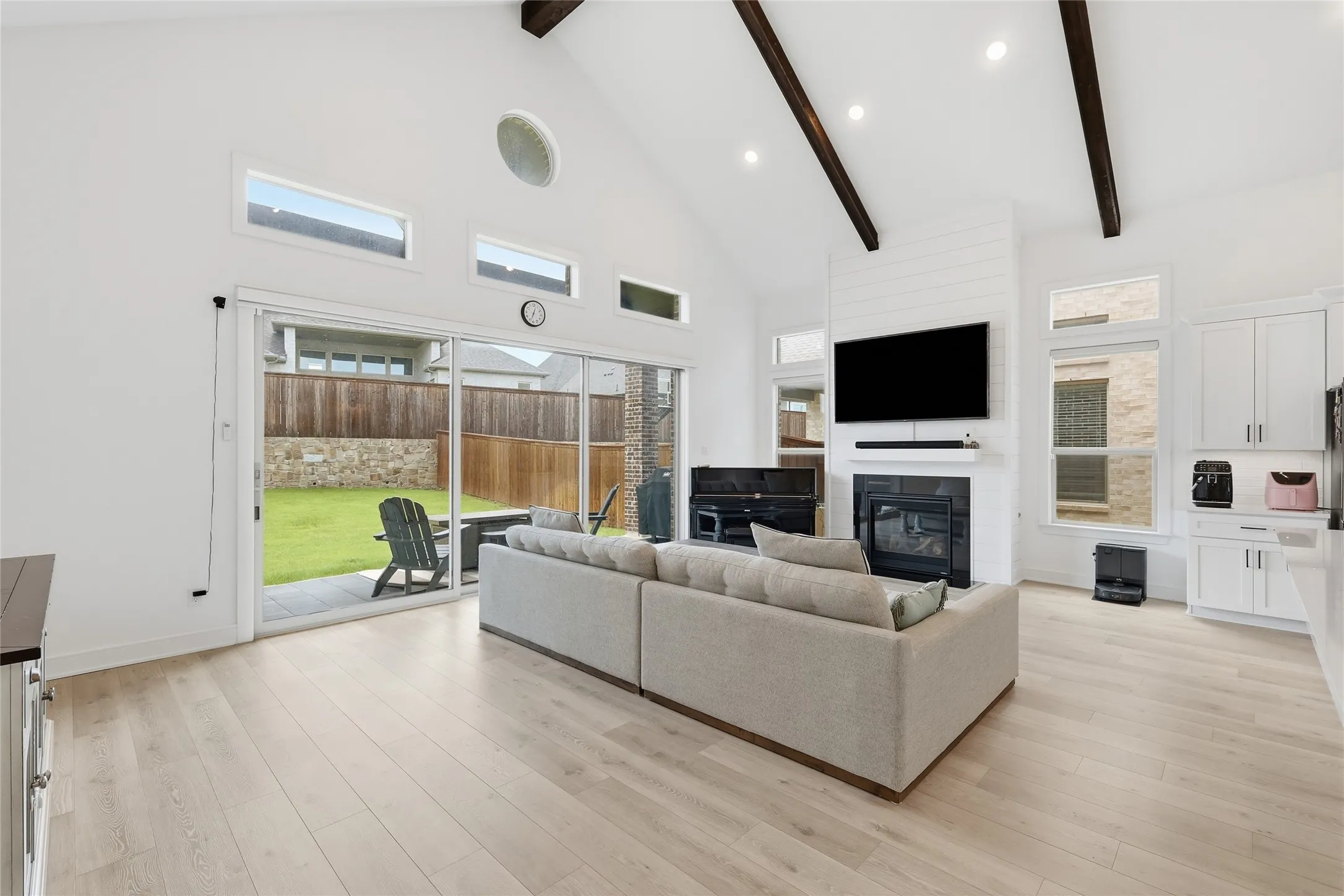 Spacious living area featuring a vaulted ceiling with exposed wood beams, light wood-finish flooring, and a fireplace with shiplap detailing