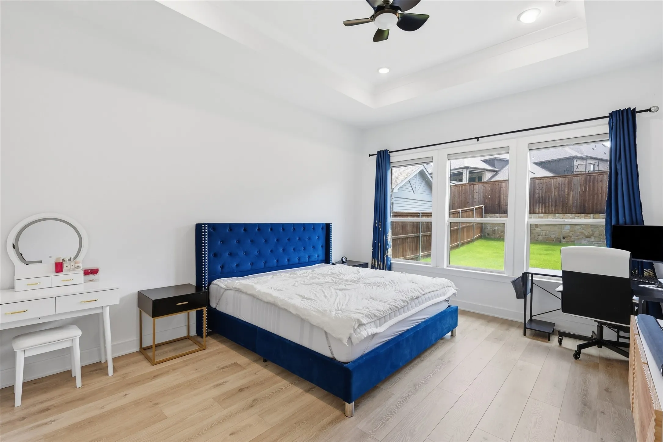 Spacious room featuring wood-finish flooring, a tray ceiling, and a ceiling fan with integrated lighting